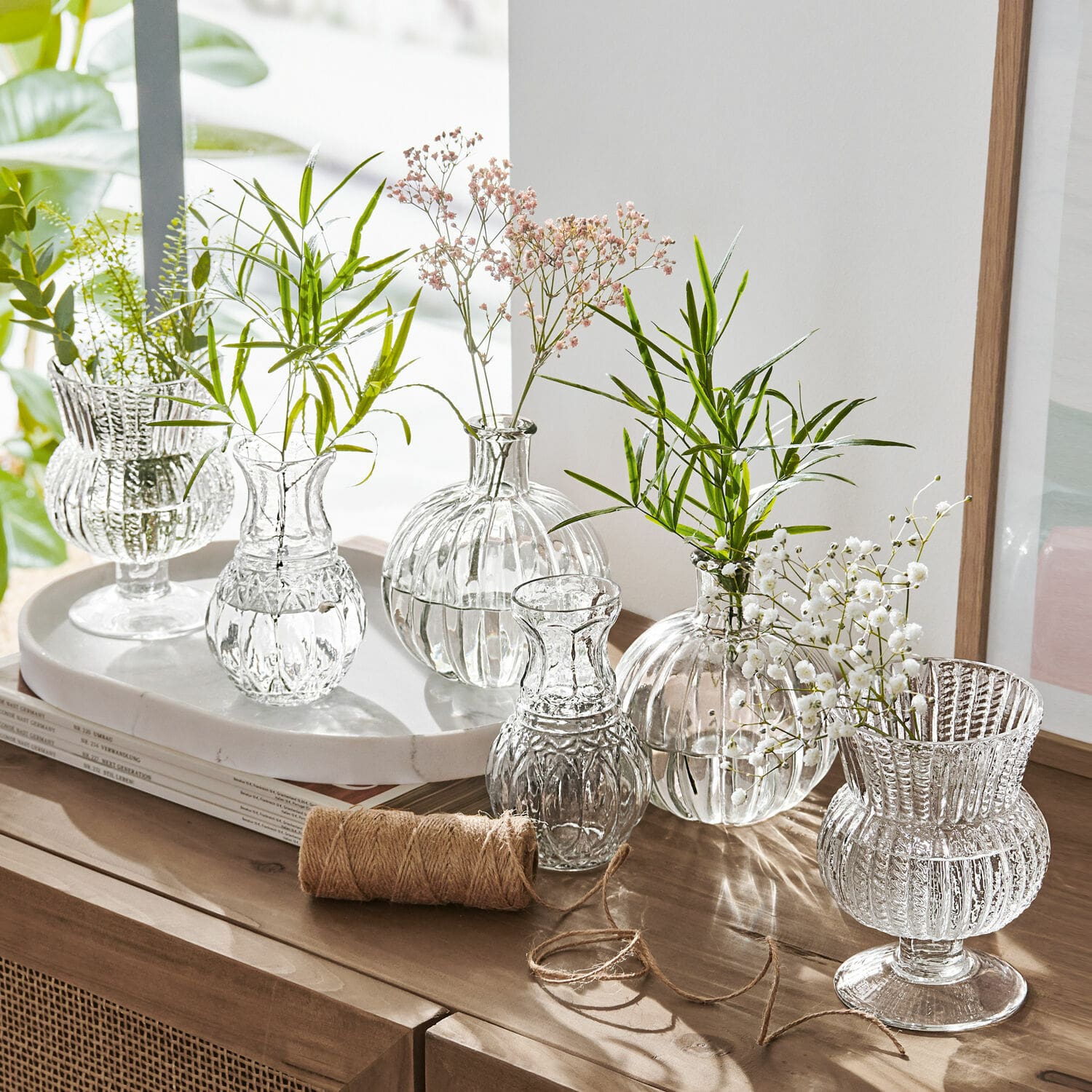 Vase 6er Set Amber Set aus transparenten Glasvasen mit grünen und weißen Blumen auf Holzkommode