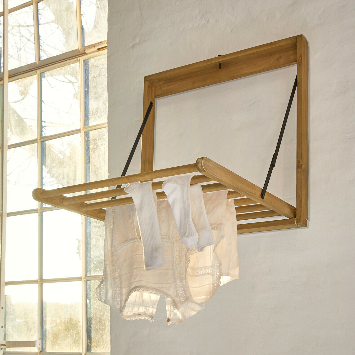 Wandklappbarer Wäscheständer aus hellem Holz mit weißen Kleidungsstücken in hellem Raum