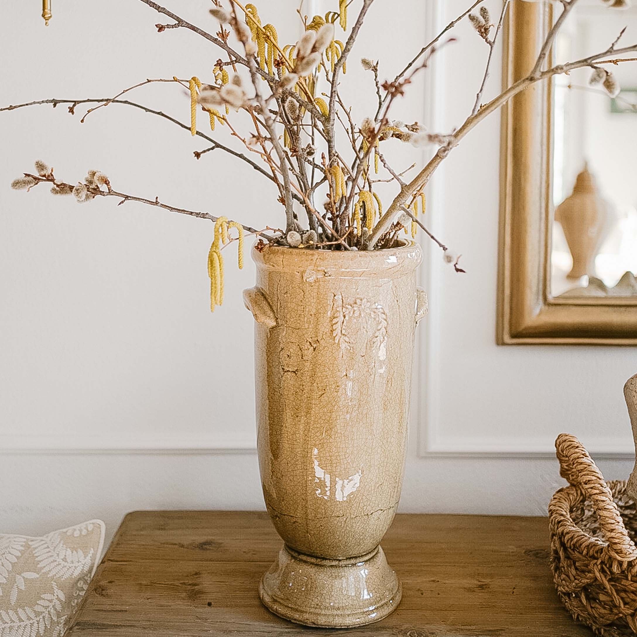 Beiger Keramikvase mit Blumen und Zweigen auf Holztisch in hellem Raum