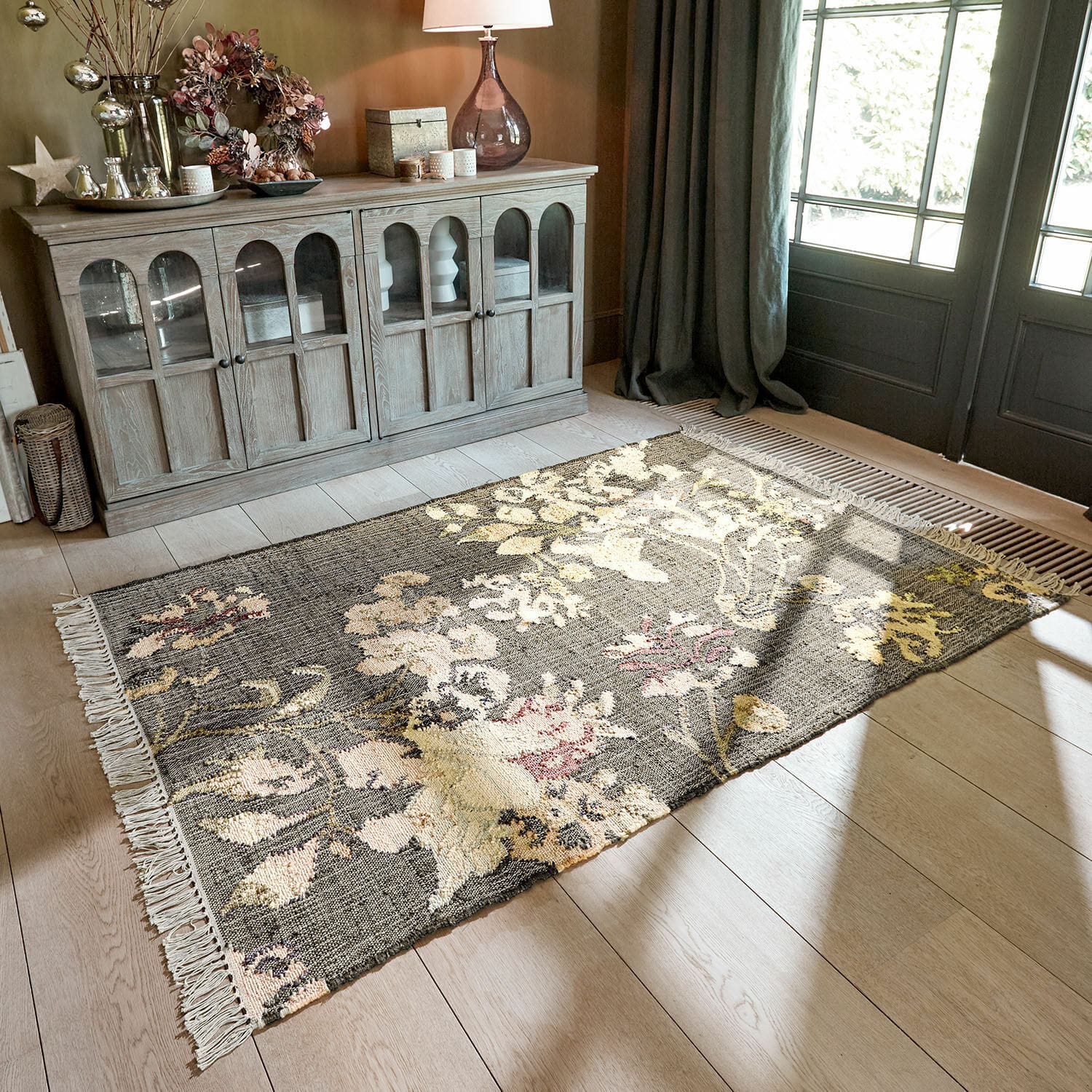 Teppich Yasirah Floral gemusterter Teppich in Grau- und Beigetönen auf hellem Holzboden im Wohnzimmer