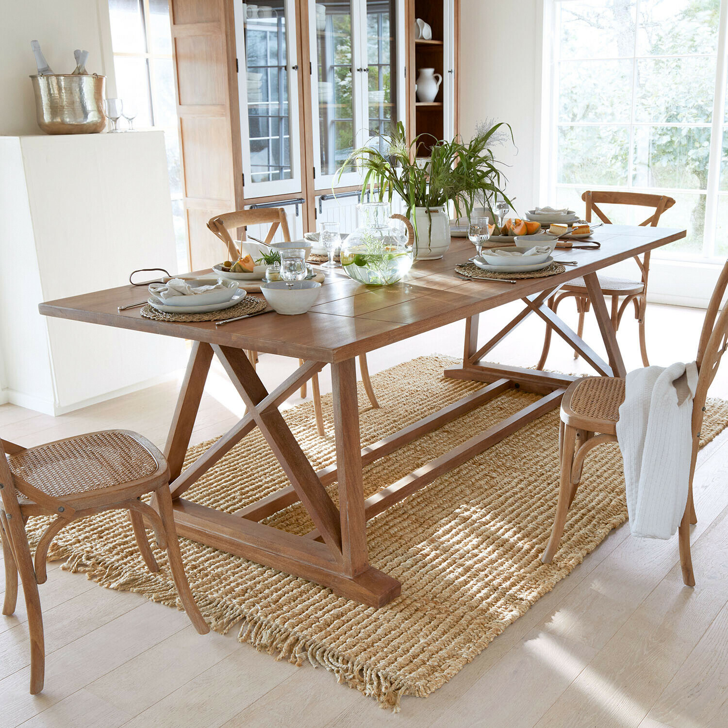 Tisch Isaverny Holz-Esstisch mit Stühlen und Naturteppich in hellem Raum, gedeckter Tisch mit Dekoration