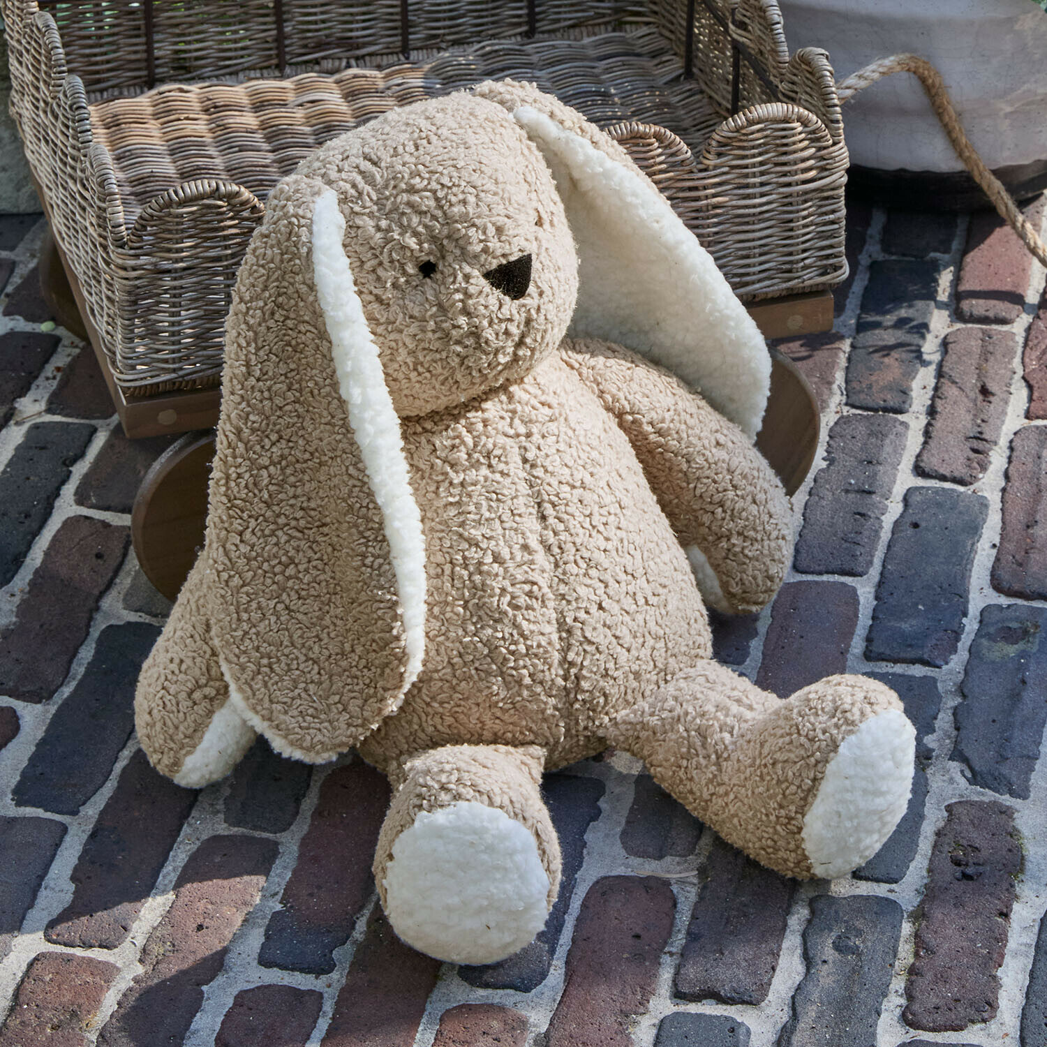 Weicher Plüschhase in Beige mit weißen Ohren und Pfoten auf gepflastertem Boden