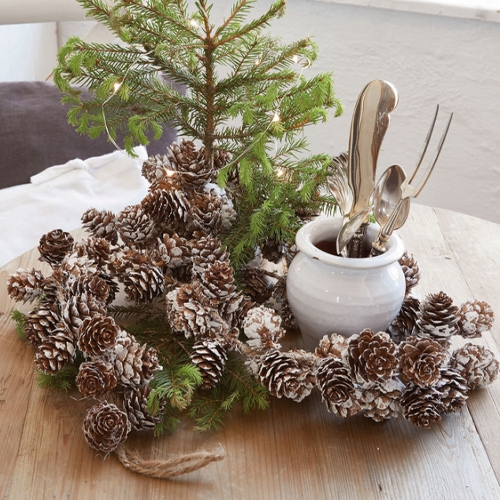 Dekorativer Zapfenkranz mit Schneeeffekt auf Holztisch, natürliche Weihnachtsdekoration