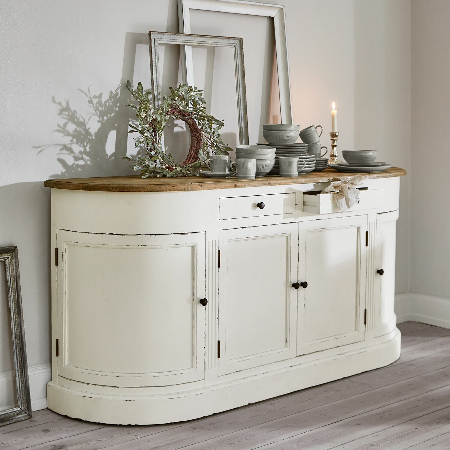 Sideboard Louisiana Weiße Holzkommode mit Holzplatte und grauem Geschirr darauf, Wanddekorationen im Hintergrund