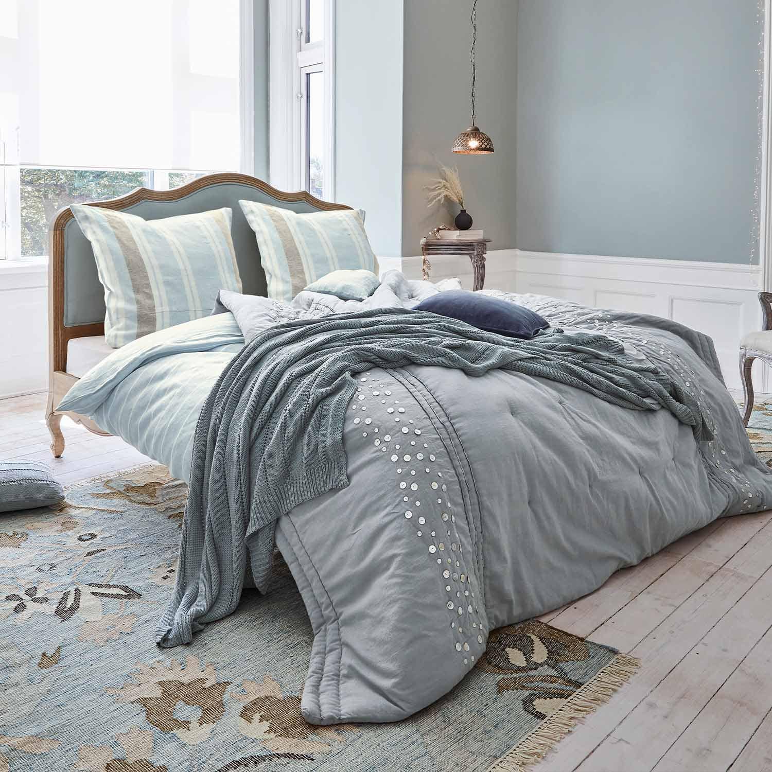 Holzbettrahmen mit gepolstertem Kopfteil, hellblaue Bettwäsche und weiche gestrickte Decke