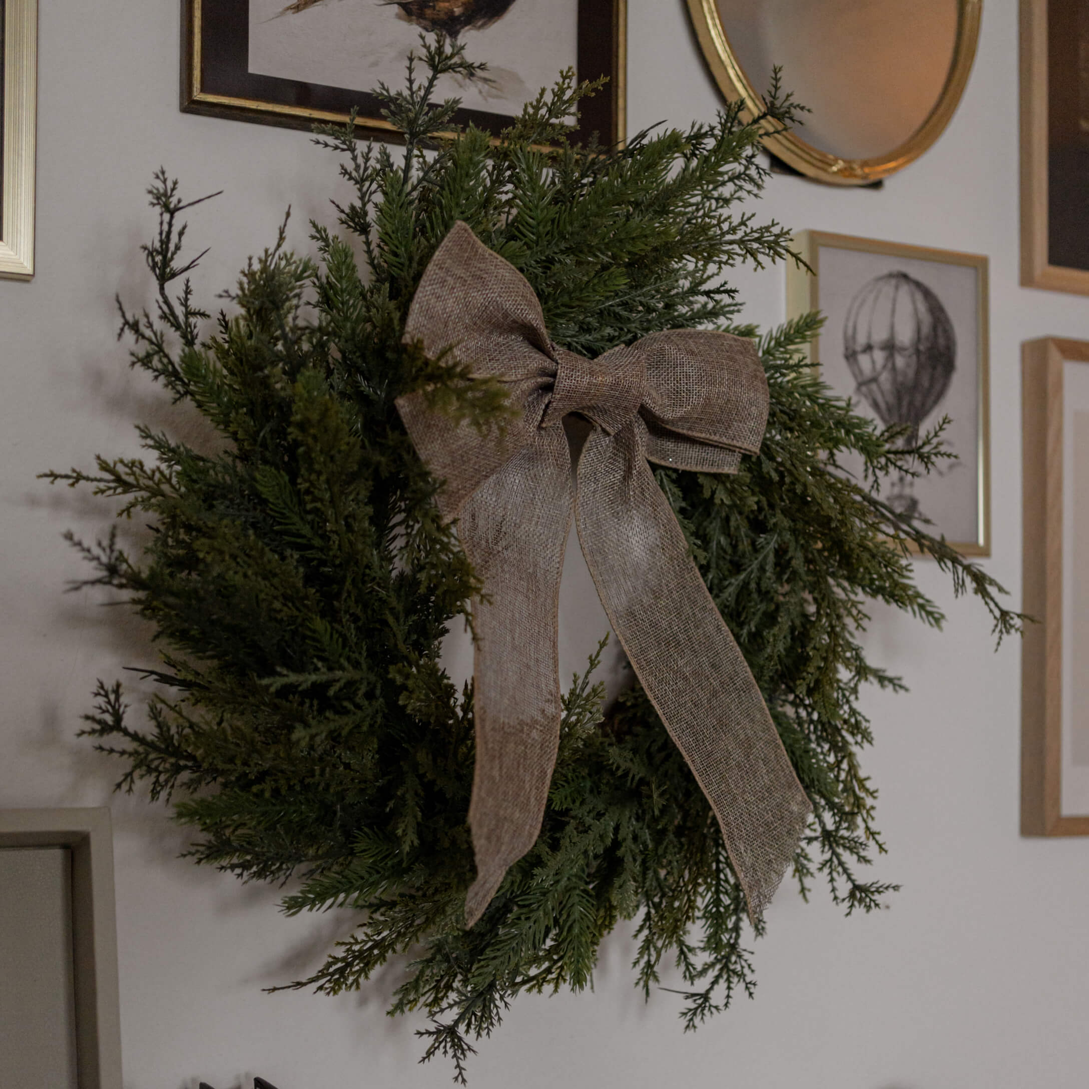 Dekorativer Kranz aus grünen Zweigen mit brauner Juteschleife an der Wand im Wohnzimmer