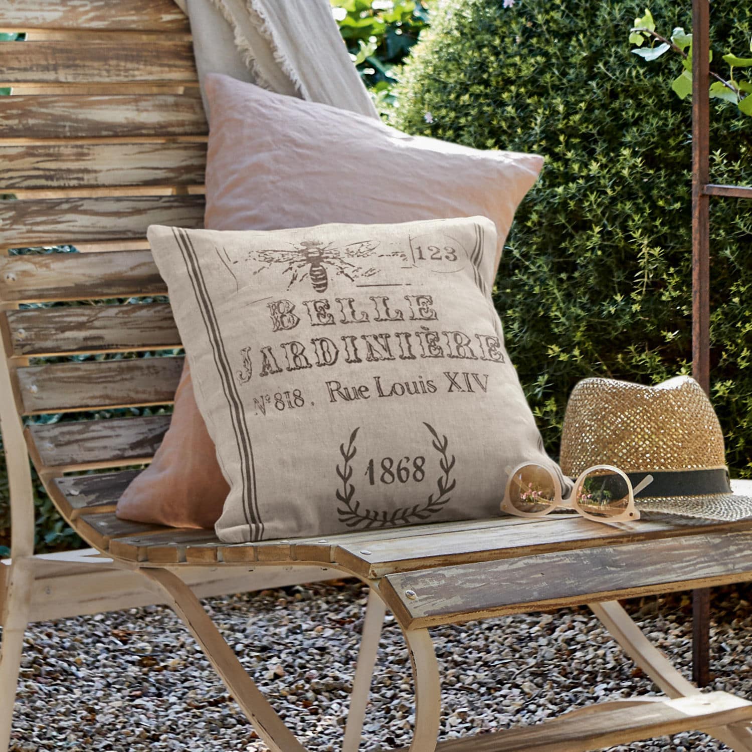 Kissenhülle Abelle Beige Leinenkissen mit Vintage-Druck auf verwitterter Holzbank im Garten mit Sonnenhut und Brille