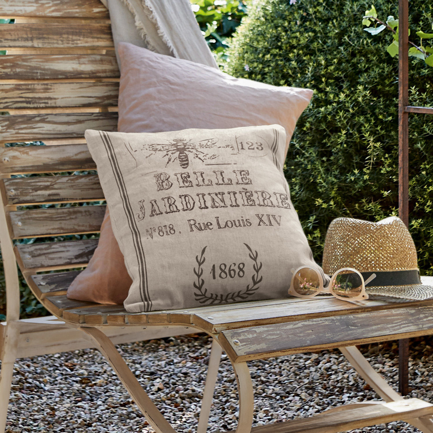 Kissenhülle Abelle Beige Leinenkissen mit Vintage-Druck auf verwitterter Holzbank im Garten mit Sonnenhut und Brille