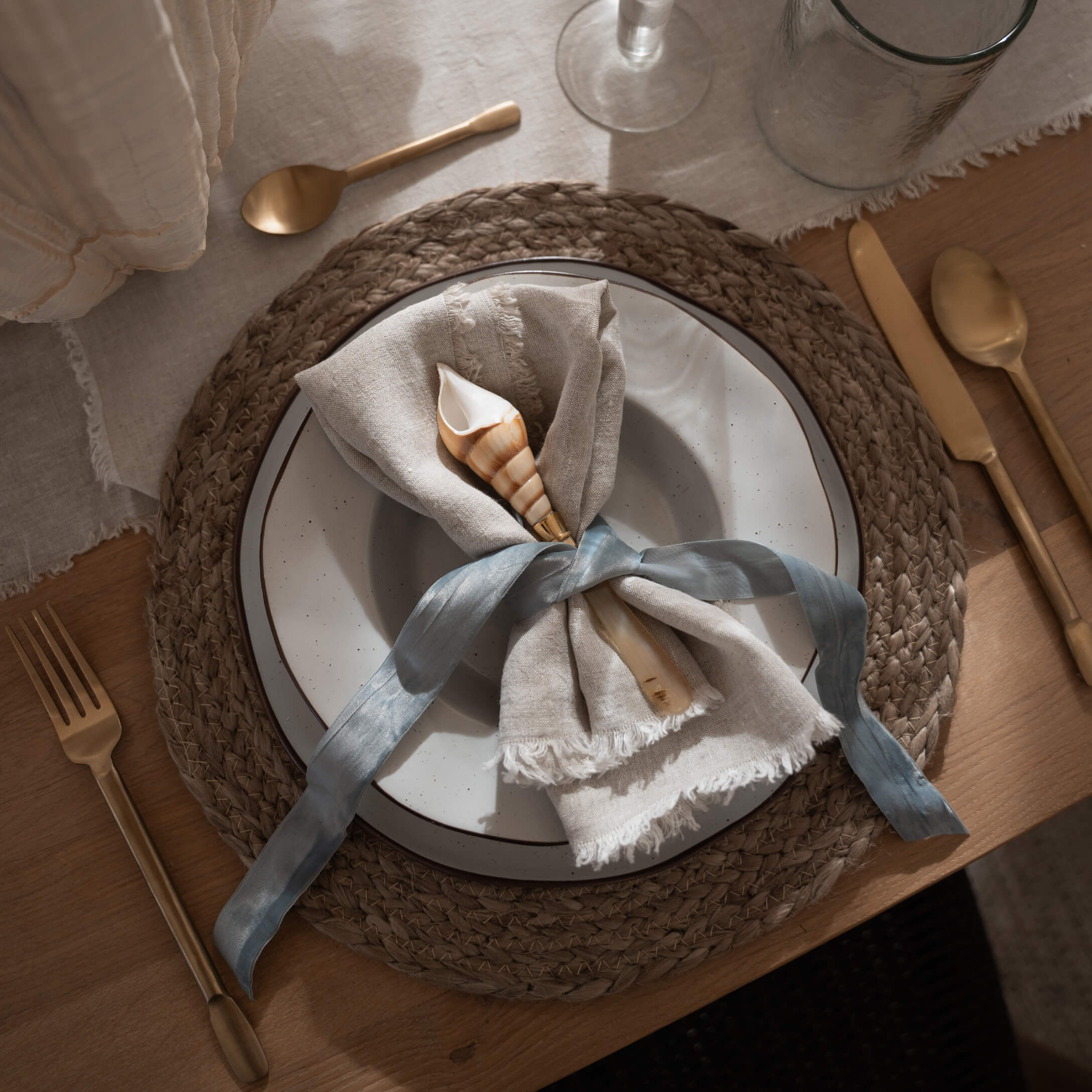 Rustikales Geschirr mit Leinenserviette und Muschel auf geflochtenem Naturmaterial-Untersetzer