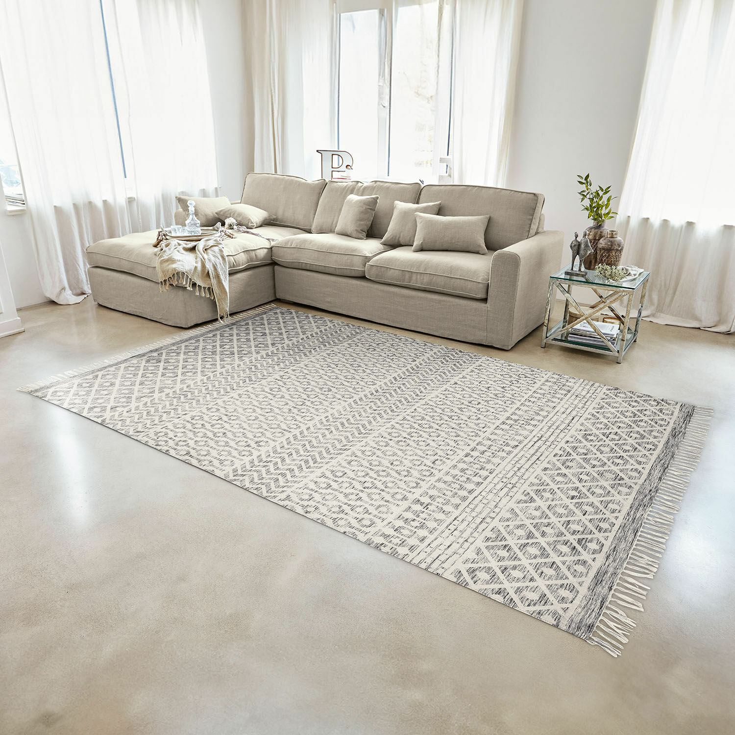 Beiges Ecksofa aus Stoff in hellem Wohnzimmer mit gemustertem Teppich und Glastisch