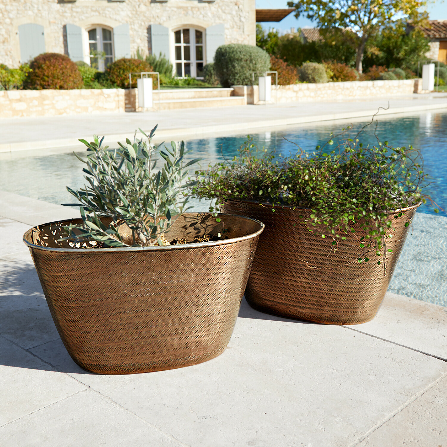 Zwei kupferfarbene Pflanzkübel mit Pflanzen neben Pool auf steinerner Terrasse, Gartendekor