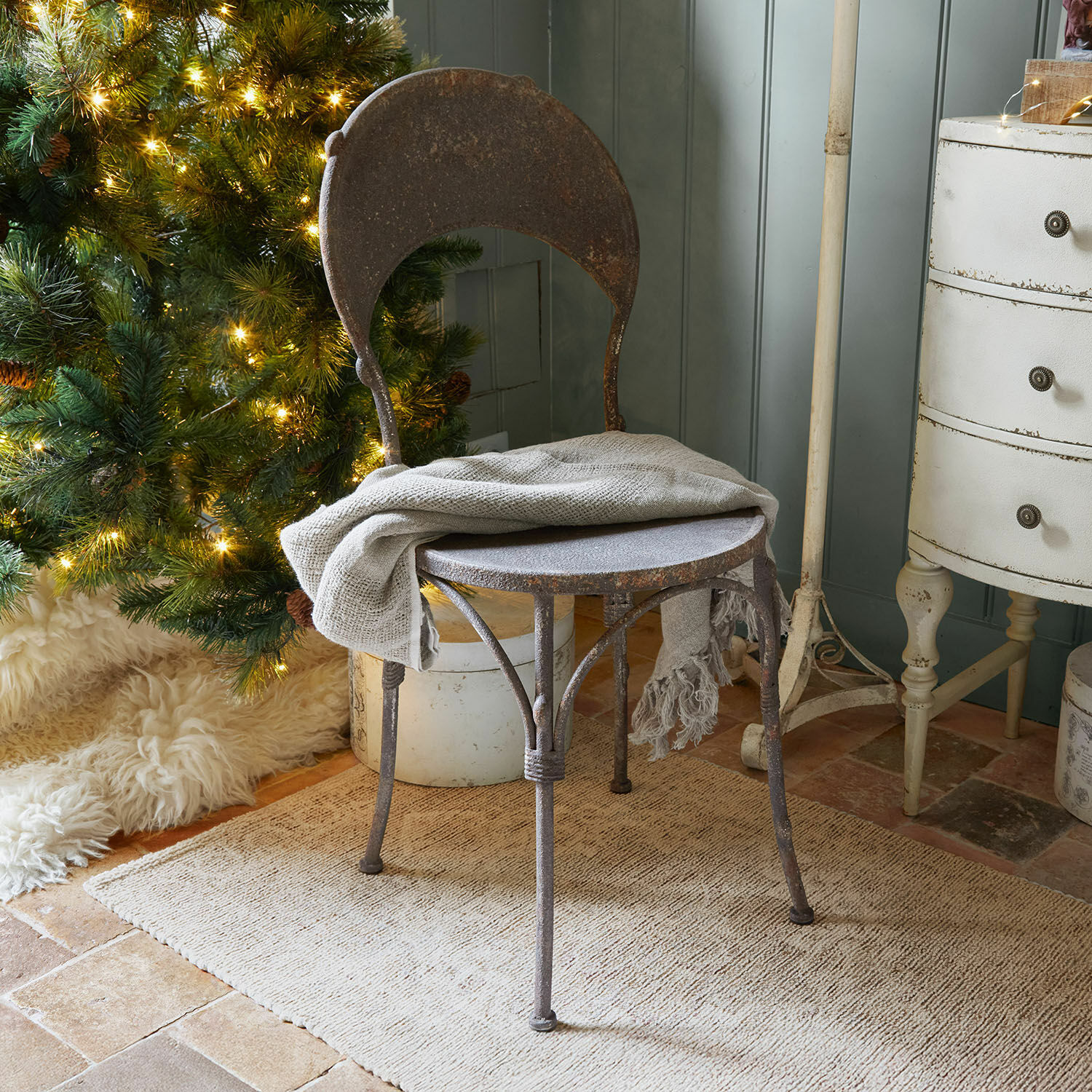 Stuhl Delivora Rustikaler Metallstuhl in Rostoptik mit grauem Plaid vor beleuchtetem Weihnachtsbaum und Teppich