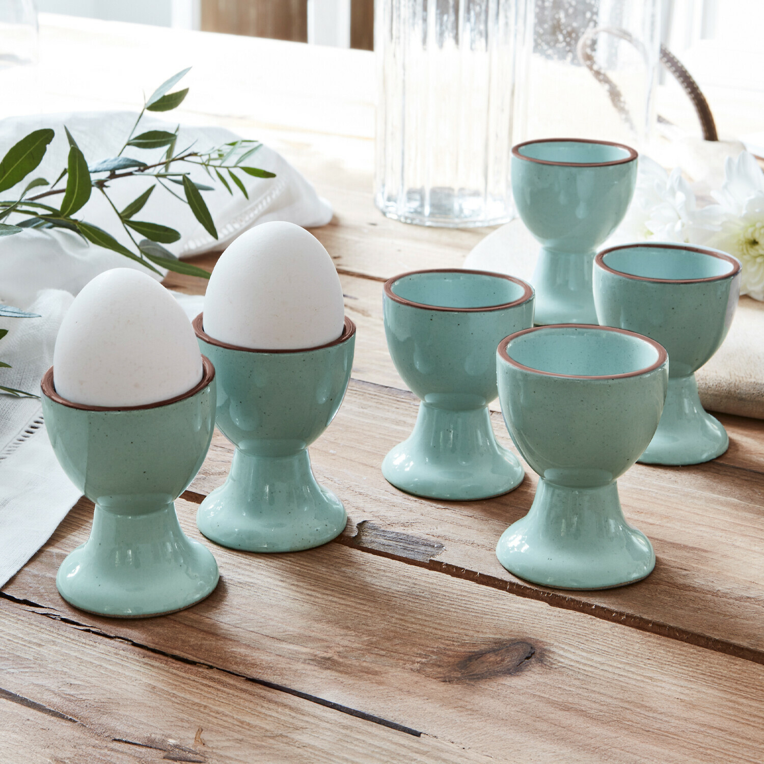 Eierbecher 6er Set Biarré Sechsteiliges Set hellblaue Keramik-Eierbecher mit braunem Rand auf rustikalem Holztisch