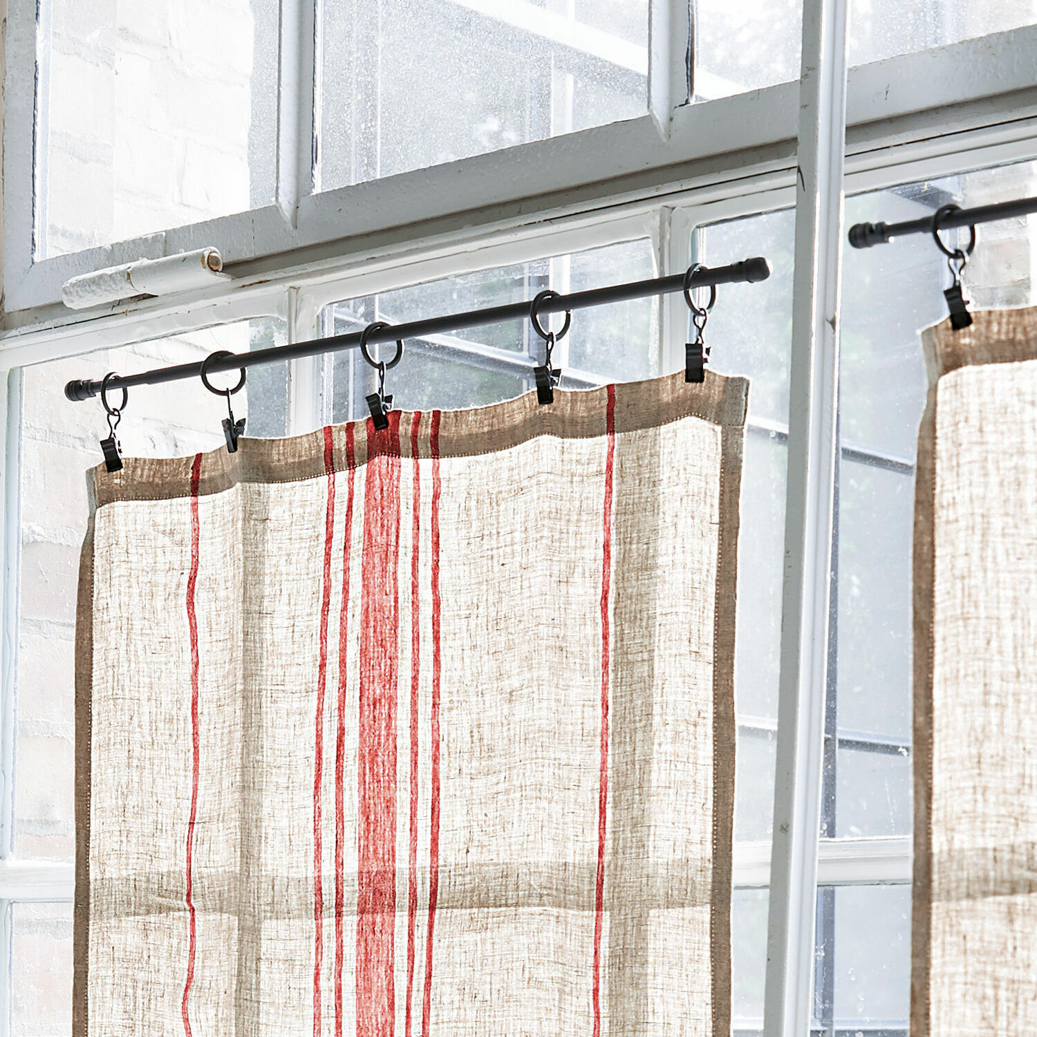 Leinenvorhang in Naturfarbe mit roten Streifen an Metallstange vor Fenster hängend