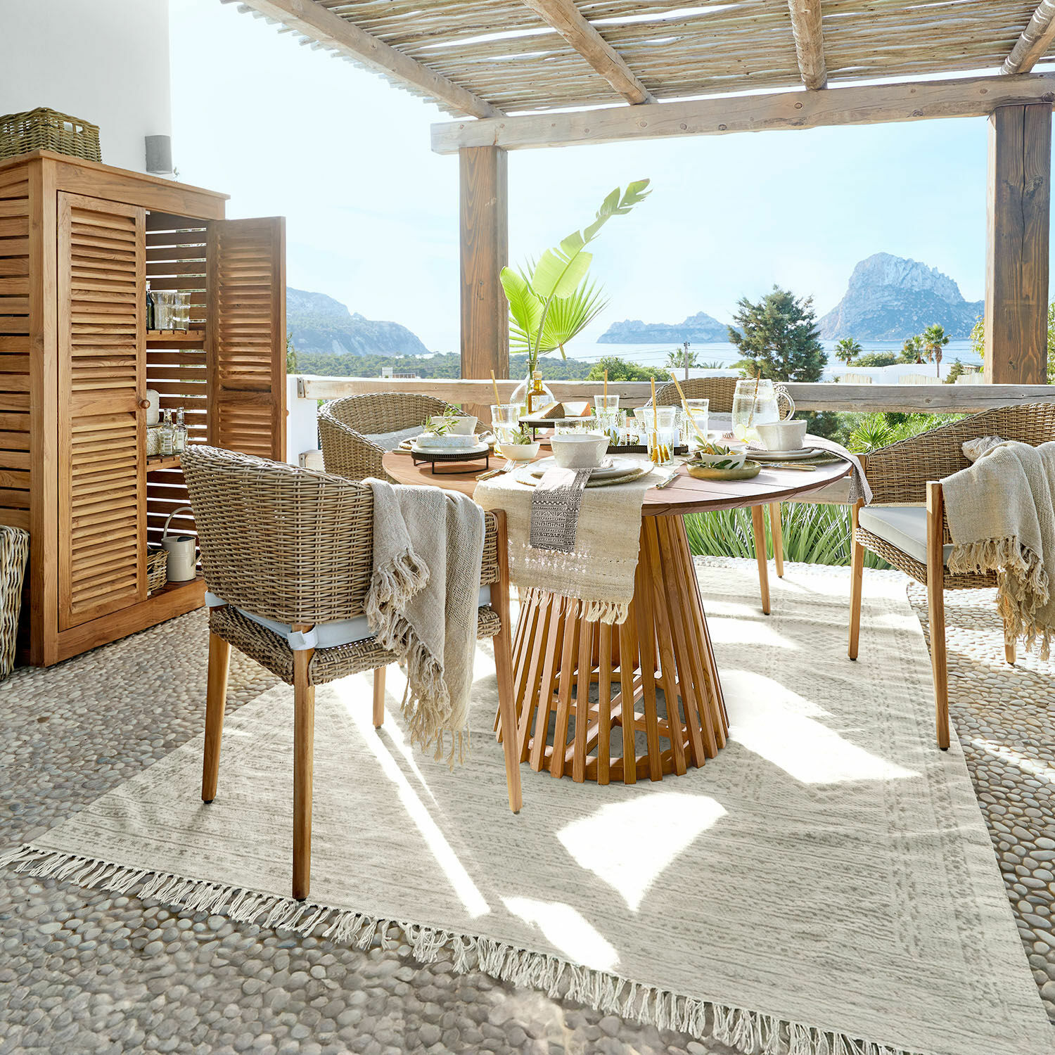 In- & Outdoor-Teppich Savagnac Terrassen-Essbereich mit rundem Holztisch und beigen Rattanstühlen, Meerblick und natürlicher Dekor