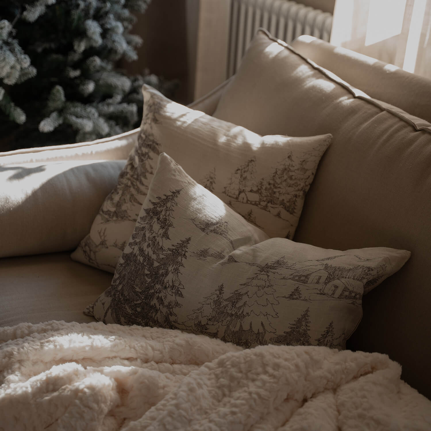 Beiges Sofa mit dekorativen Kissen im Waldmotiv und weicher cremefarbener Decke im Wohnzimmer