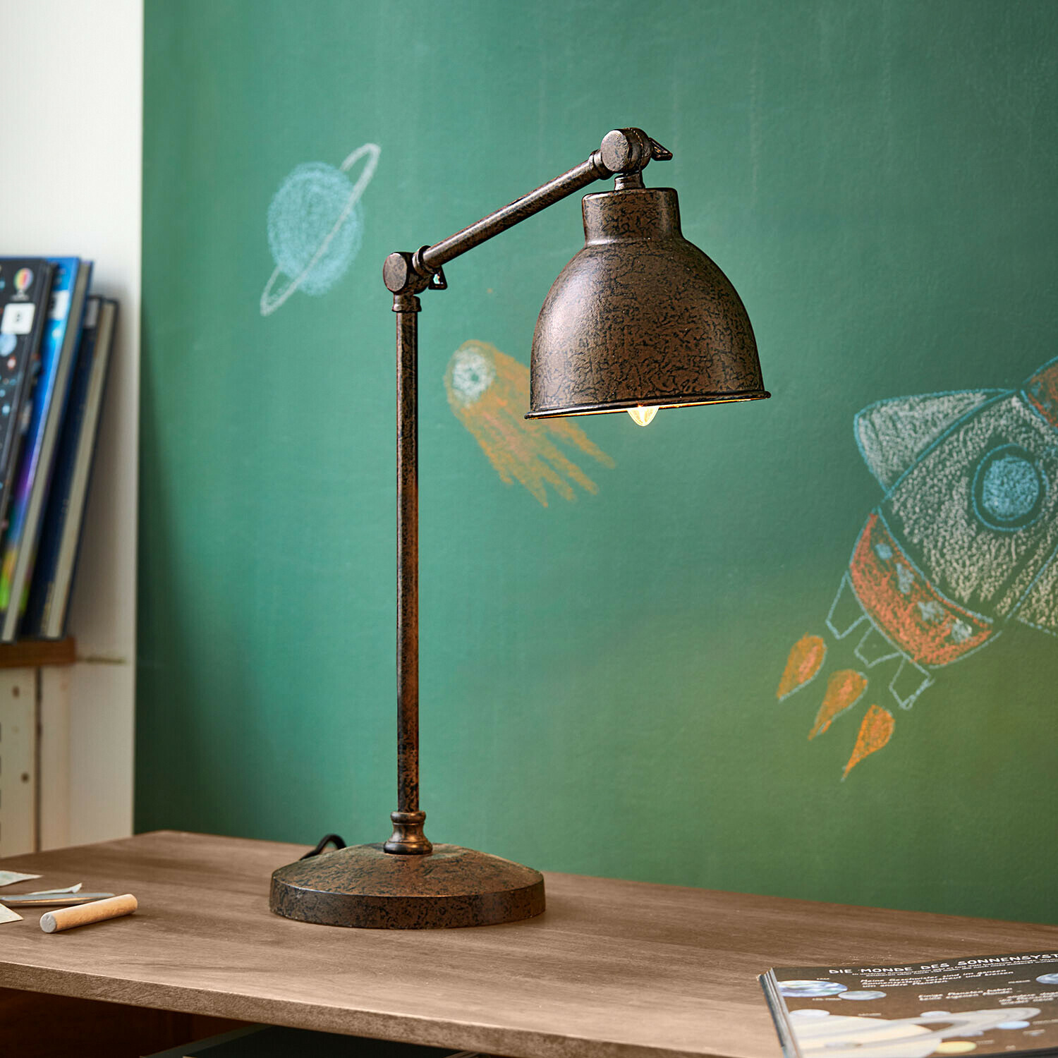 Schreibtischlampe Cheeklee Vintage Metall-Schreibtischlampe in rostbraun auf Holztisch vor grüner Tafel mit Weltraummotiven