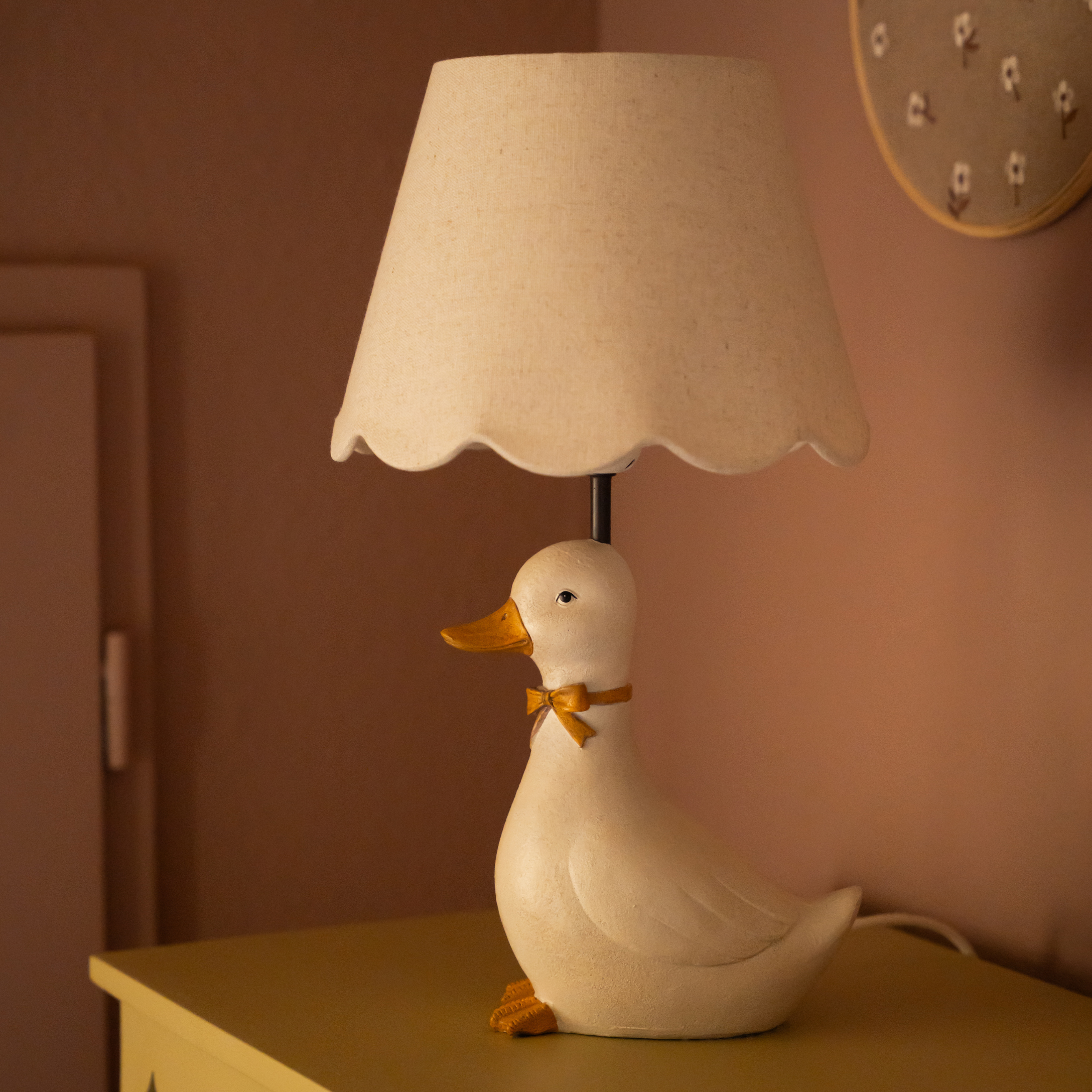Tischlampe in Entenform aus weißem Material mit beigem Lampenschirm und orangefarbener Schleife