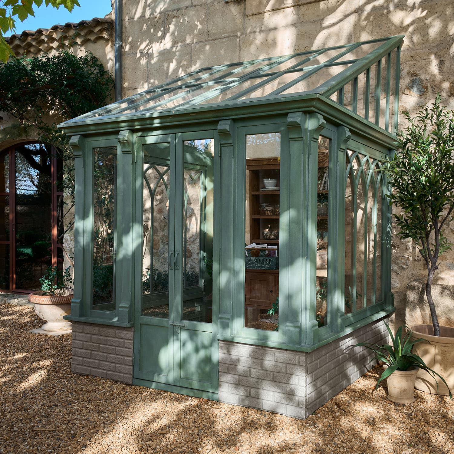 Grünes Holz-Gewächshaus mit transparentem Glasdach und Ziegelsteinbasis im Garten