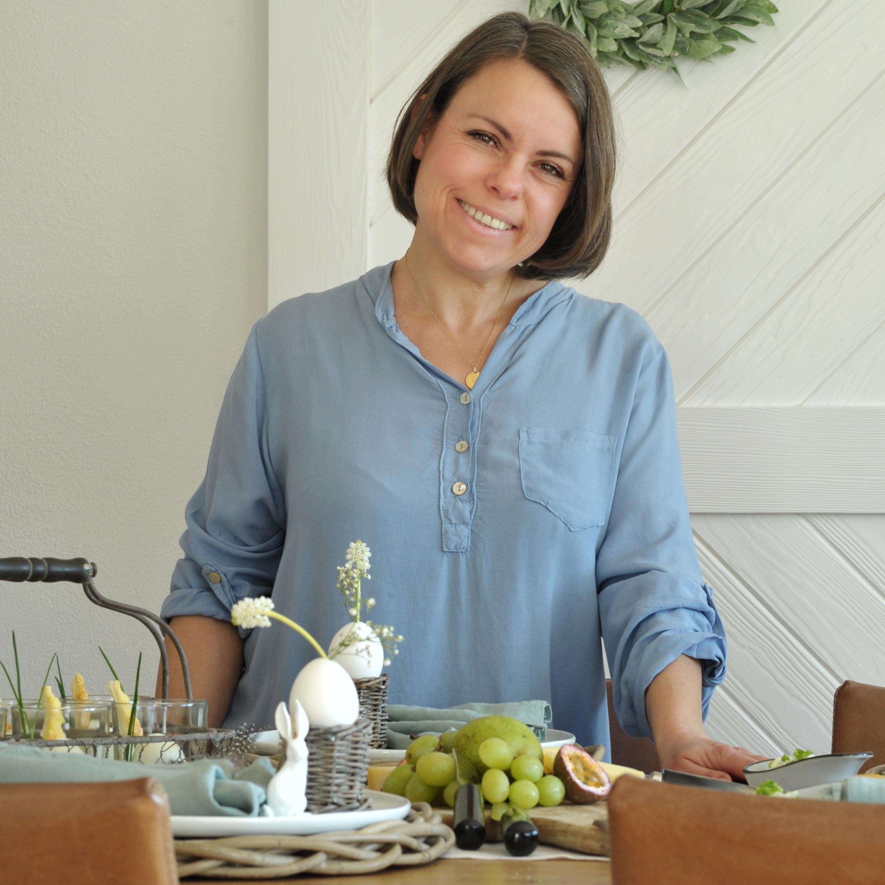 Frau in blauem Hemd am Tisch mit Osterdekoration und Obst für Brunch