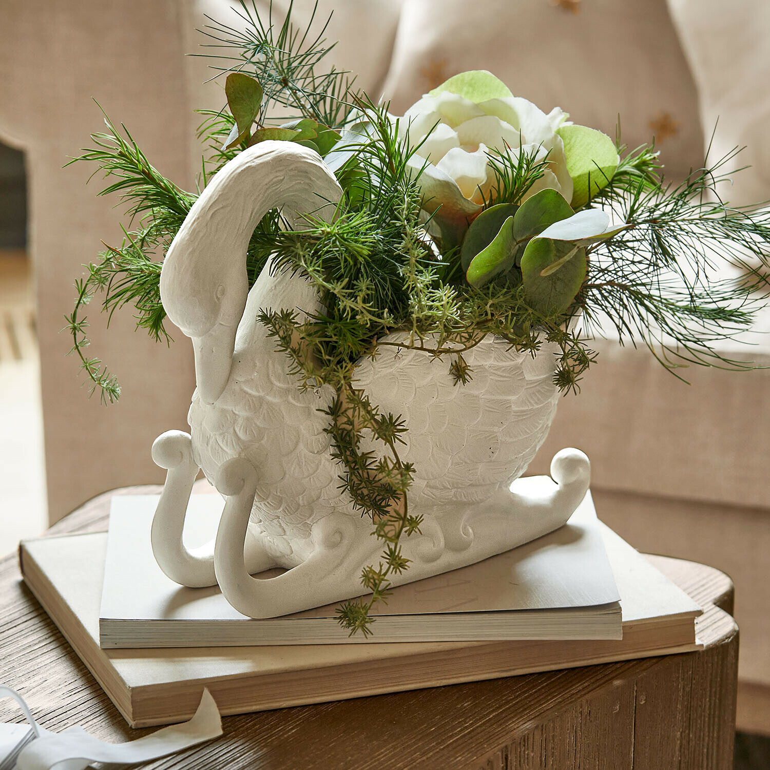 Übertopf Elarin Weißer Keramikvase in Schwanform mit grünen Pflanzen und weißen Blüten auf Holztisch