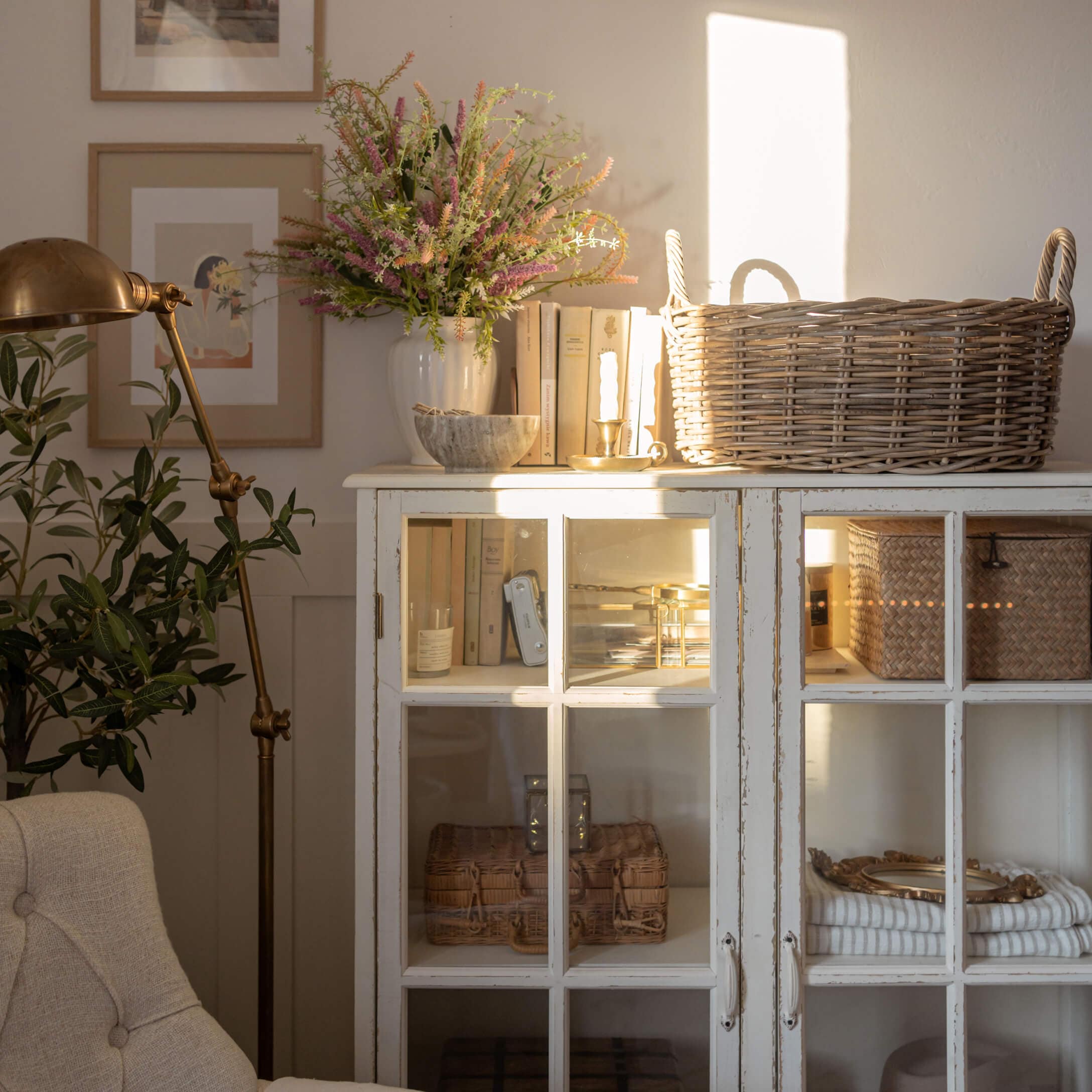 Weißer Holzschrank mit Glastüren, Korb aus Weide und Dekorationen in hellem Wohnzimmer