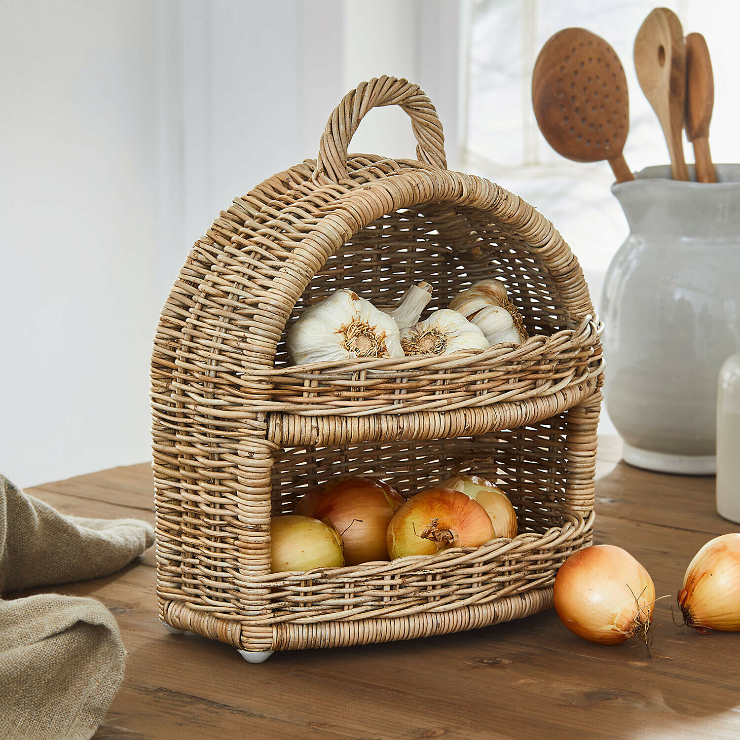 Zweistöckiger Korb aus natürlichem Rattan mit Knoblauch und Zwiebeln auf rustikalem Holztisch