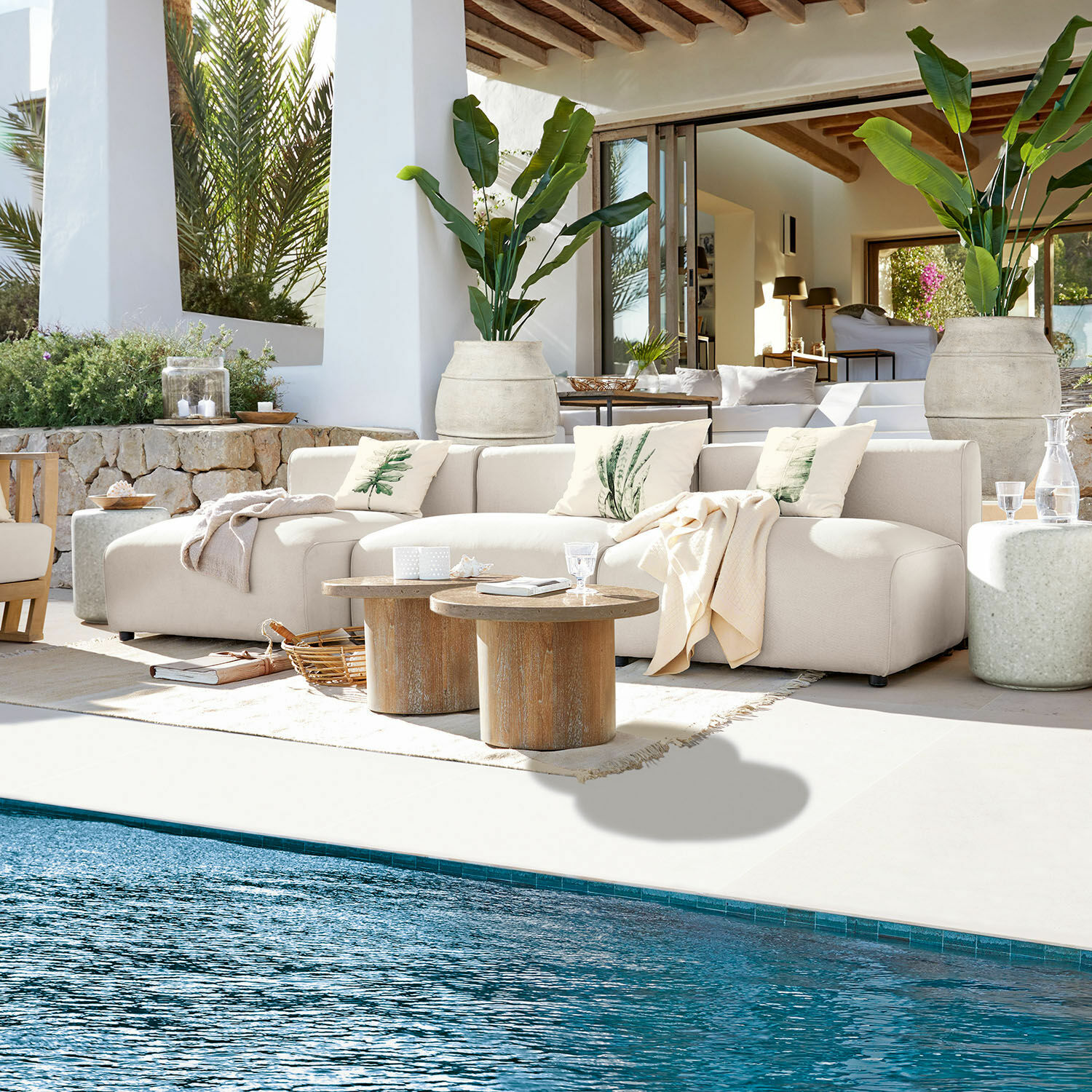 Sitzgruppe Vézère Beige Stoffsofa auf Terrasse am Pool mit Holztischen und dekorativen Kissen in natürlichem Ambiente