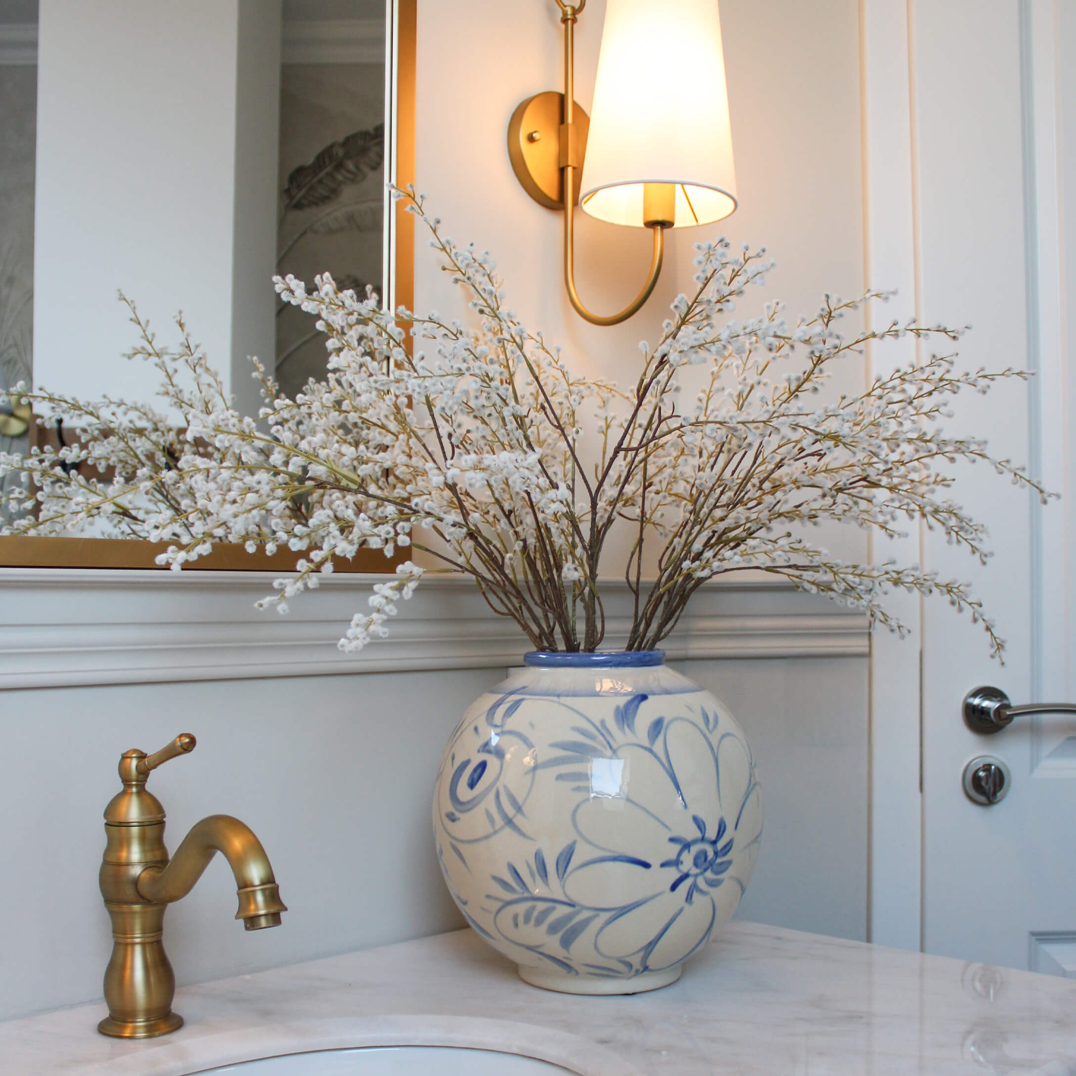 Keramikvase mit blauem Blumenmuster und weißen Blütenzweigen auf Marmor-Waschbeckenablage im Bad