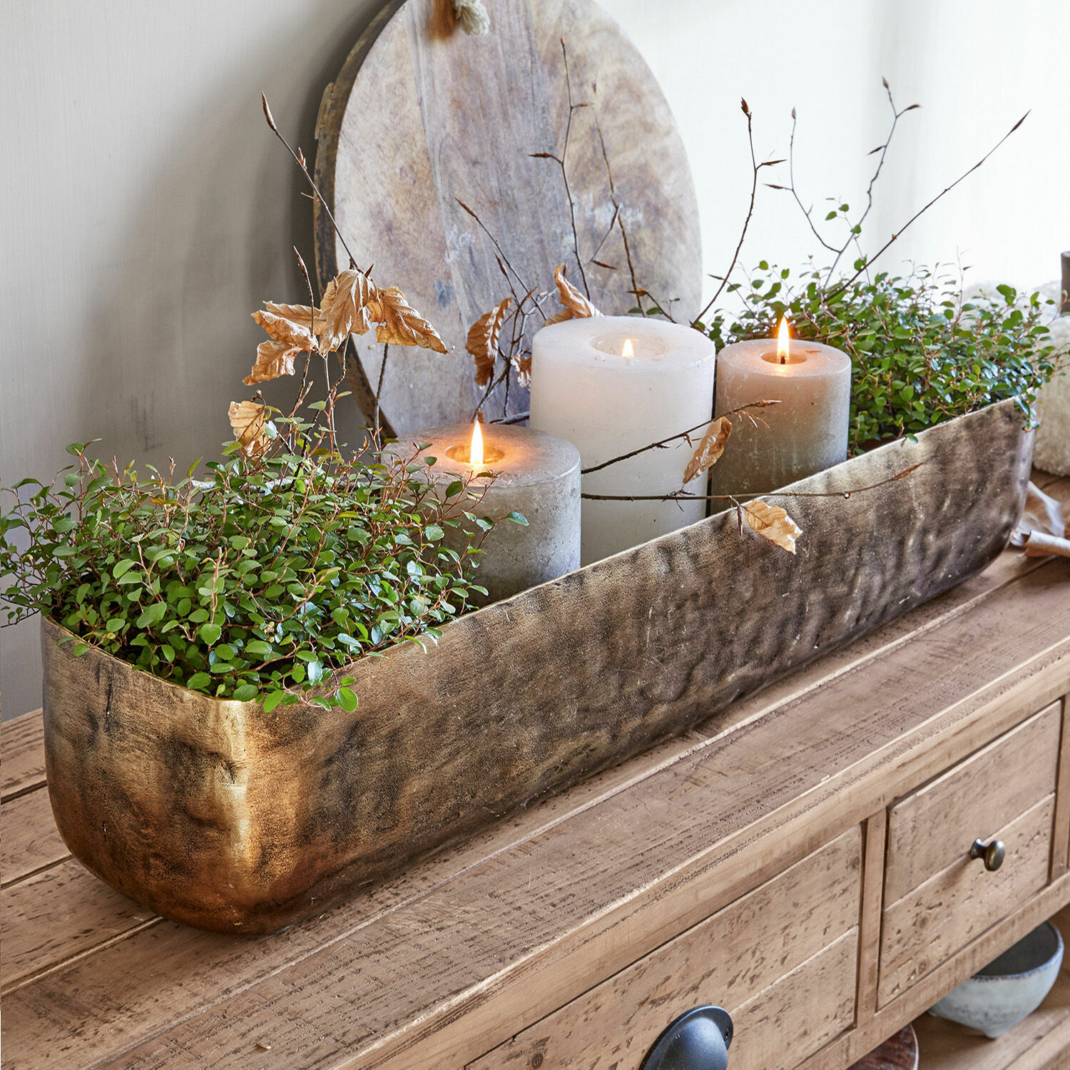 Schale Skye Dekorativer goldener Metall-Blumenkasten mit grünen Pflanzen und drei Kerzen auf Holztisch