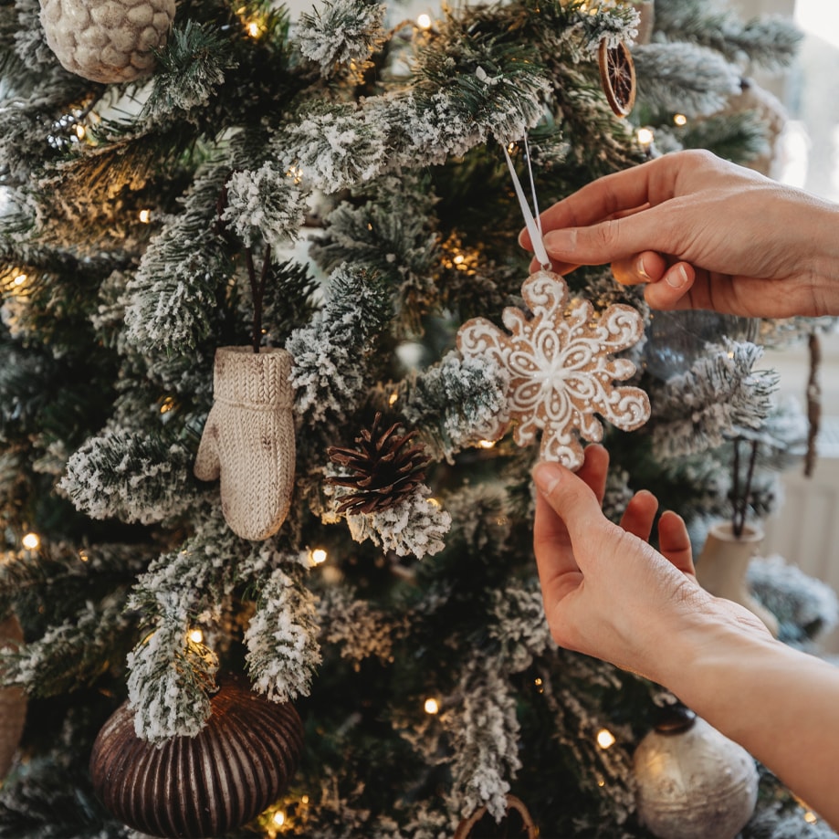 Hände hängen Schneeflockenornament an schneebedeckten Weihnachtsbaum mit Lichterkette