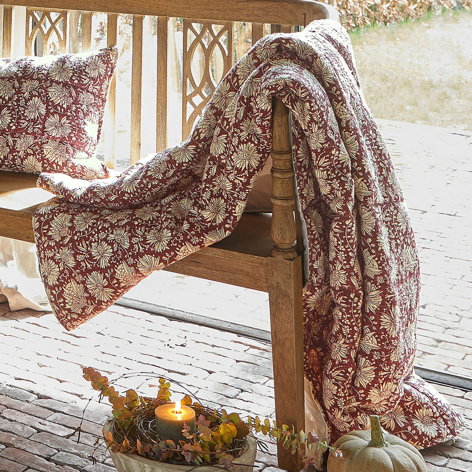 Plaid Soleique Roter Decke und Kissen mit Blumenmuster auf Holzbank, herbstliche Dekoration mit Kürbis und Kerze