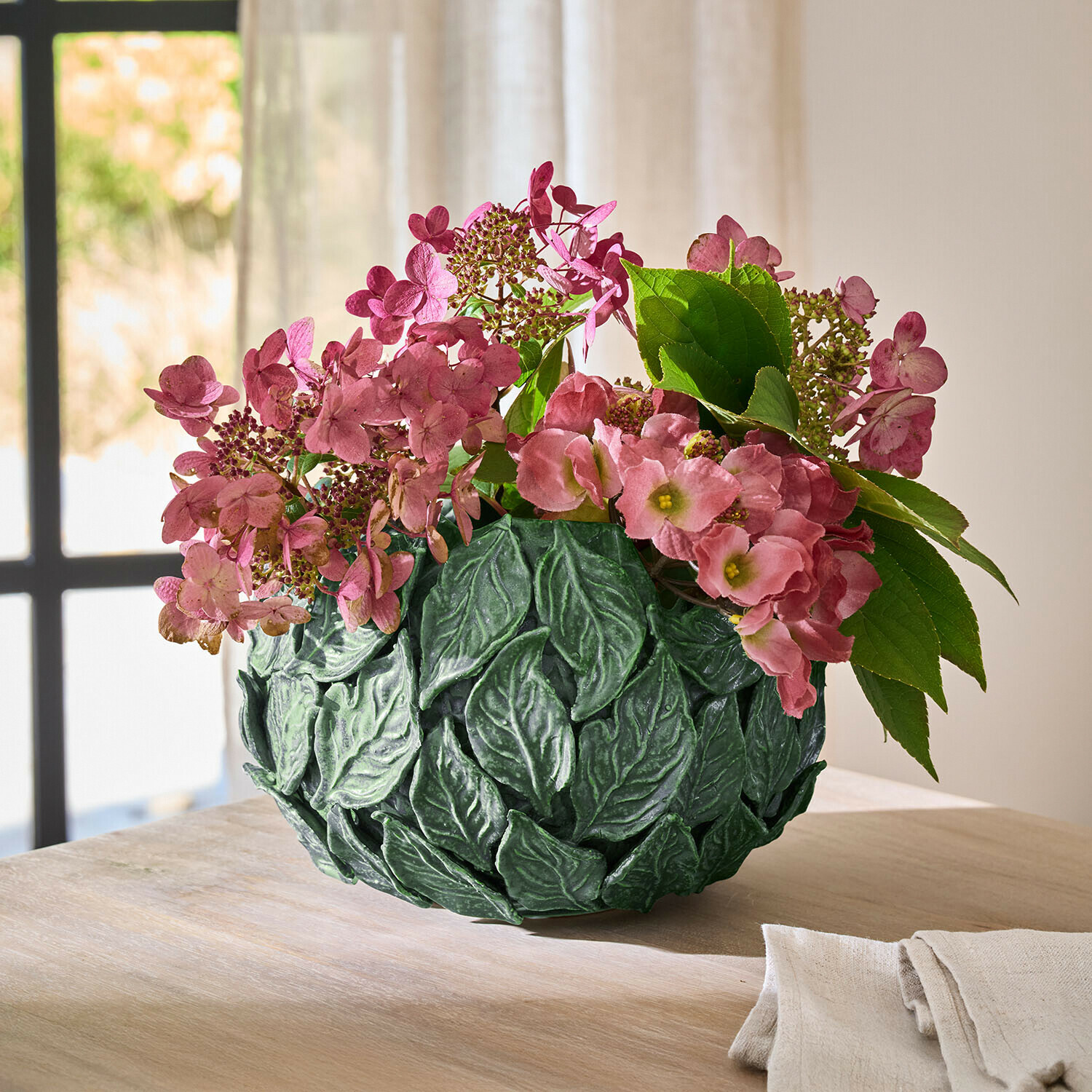 Vase Fiorabela Grüne Blatt-Dekovase mit rosa Blumen auf Holztisch in hellem Raum als Wohnaccessoire