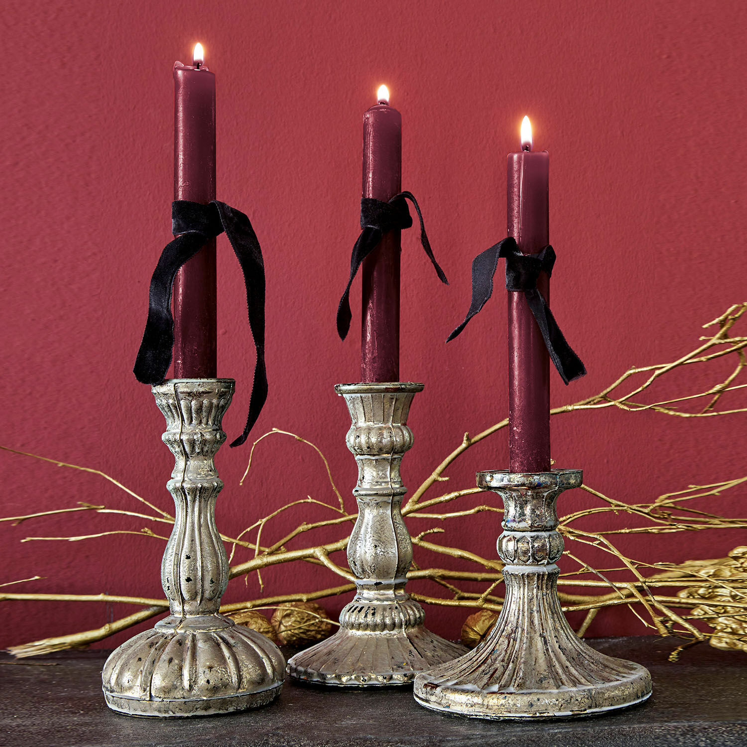 Kerzenständer 3er Set Bretagne Drei dekorative Metall-Kerzenhalter mit bordeauxfarbenen Kerzen und schwarzen Bändern vor dunklem Hintergrund