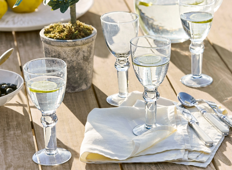 Wassergläser mit Zitrone auf Holztisch mit weißer Serviette und Besteck, mediterraner Stil