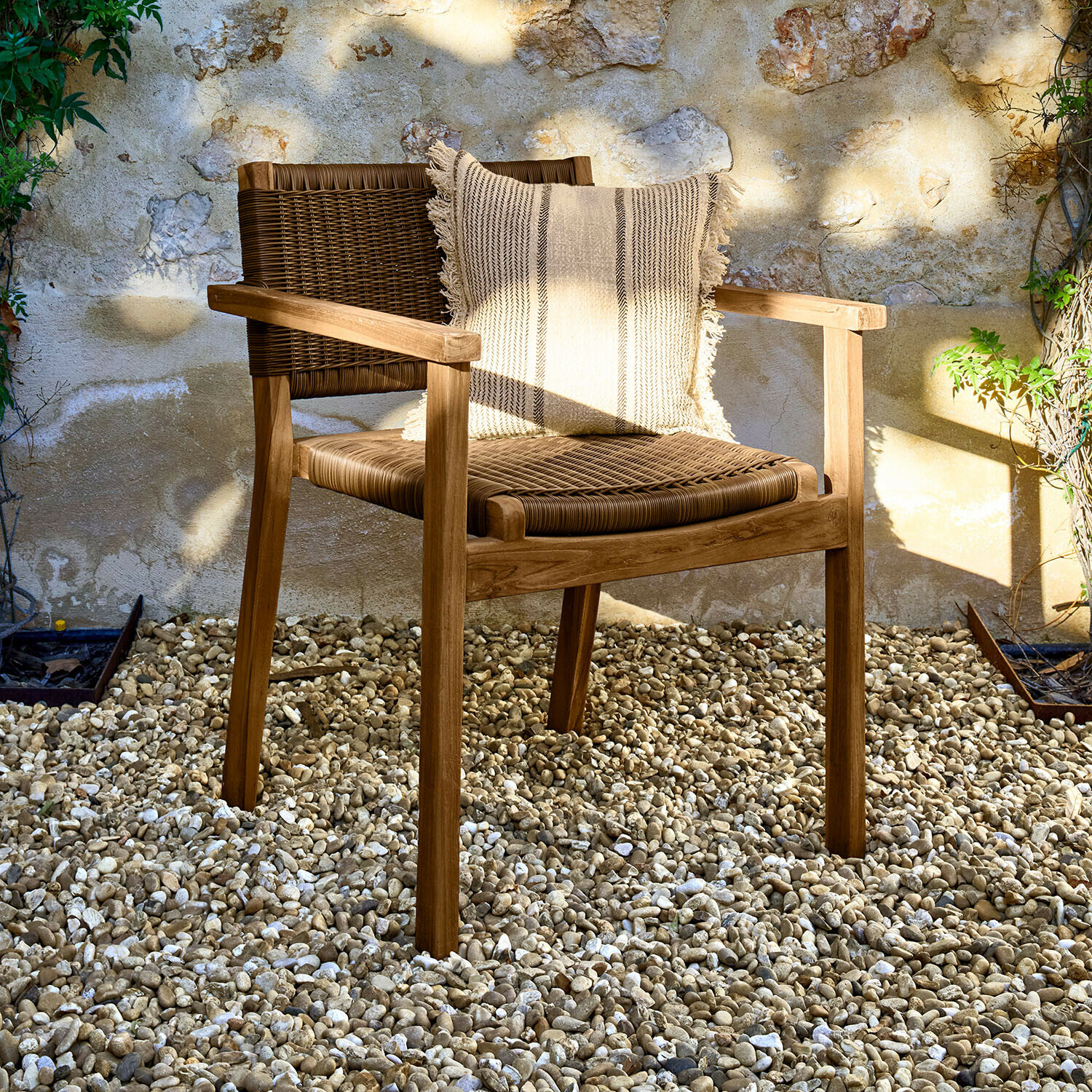 Stuhl Calvini Gartenstuhl aus Holz und Rattan in Naturtönen mit dekorativem Kissen auf hellem Kiesboden