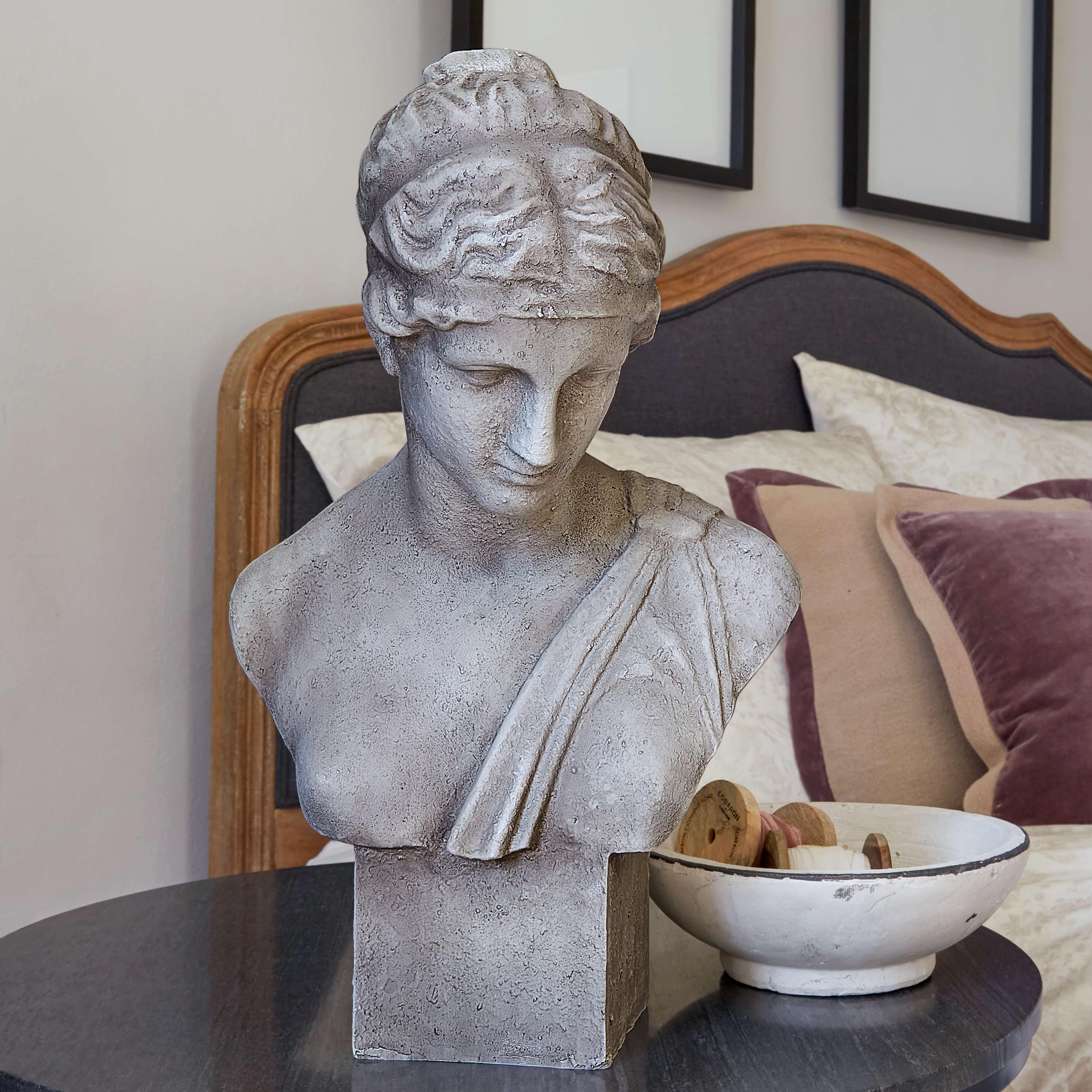 Graue Steinskulptur-Büste auf Tisch neben weißer Schale mit Holzspulen im Schlafzimmer