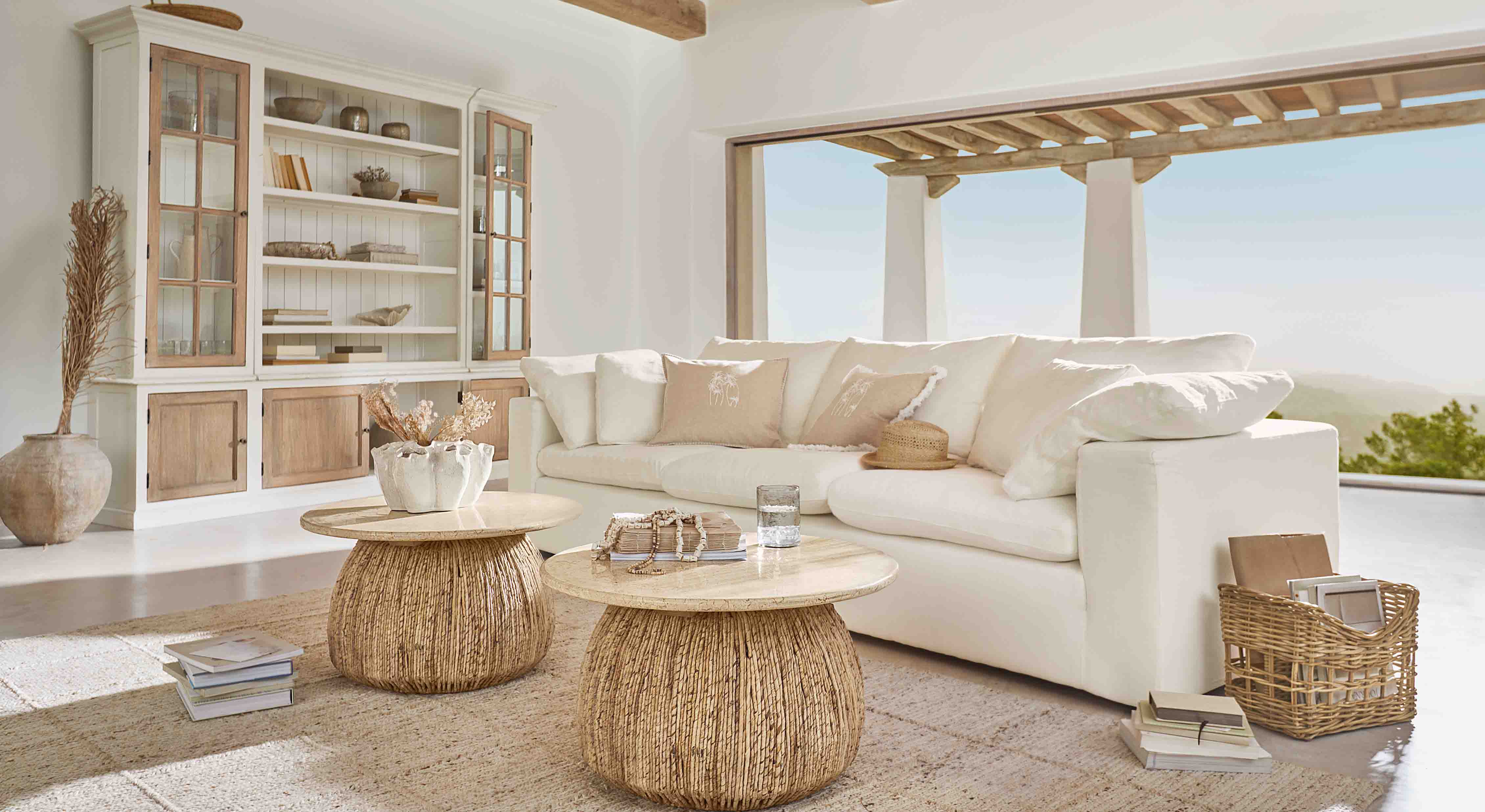Gemütliches Wohnzimmer mit weißem Sofa und zwei runden Couchtischen aus Naturholz und Rattan