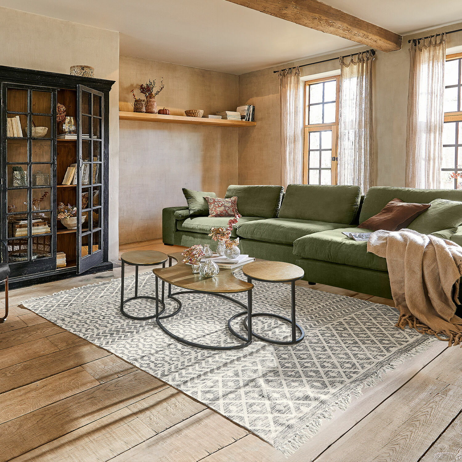 Gemütliches Wohnzimmer mit grünem Stoffsofa, Holzboden, modernem Teppich und Metall-Couchtischen