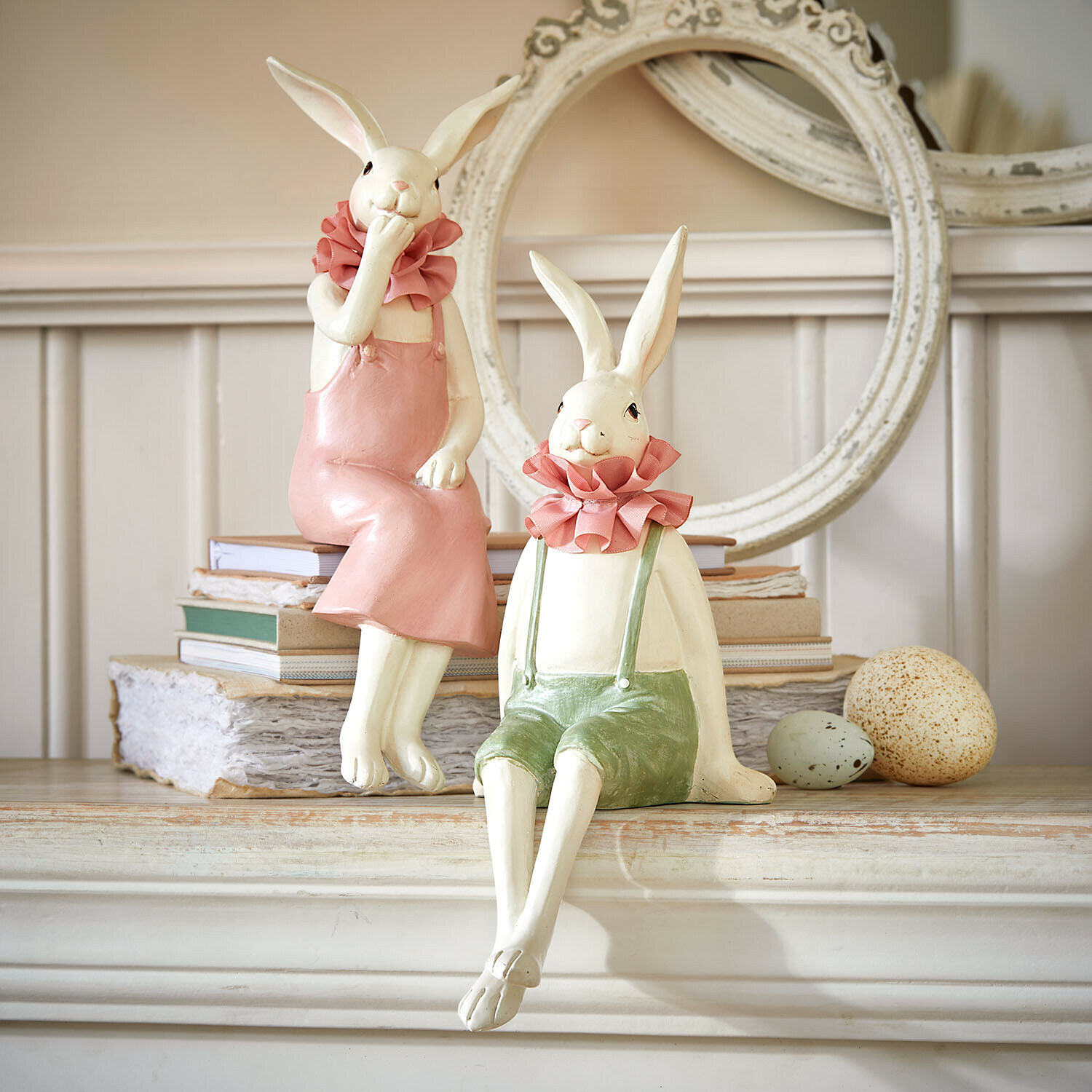 Dekorative Keramik-Hasenfiguren in pastellfarbenen Kleidern auf Kaminsims mit Büchern und Eiern