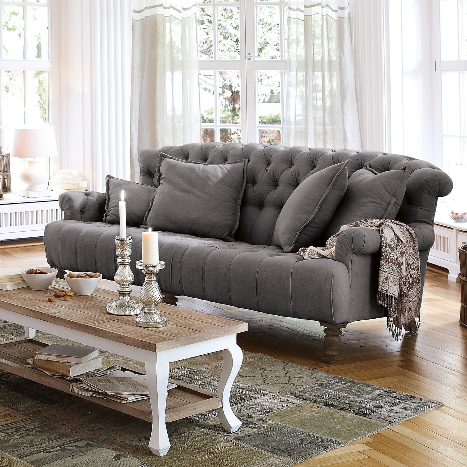 Grau gepolstertes Sofa aus Stoff mit Kissen und dekorativem Plaid in hellem Wohnzimmer mit Holzboden