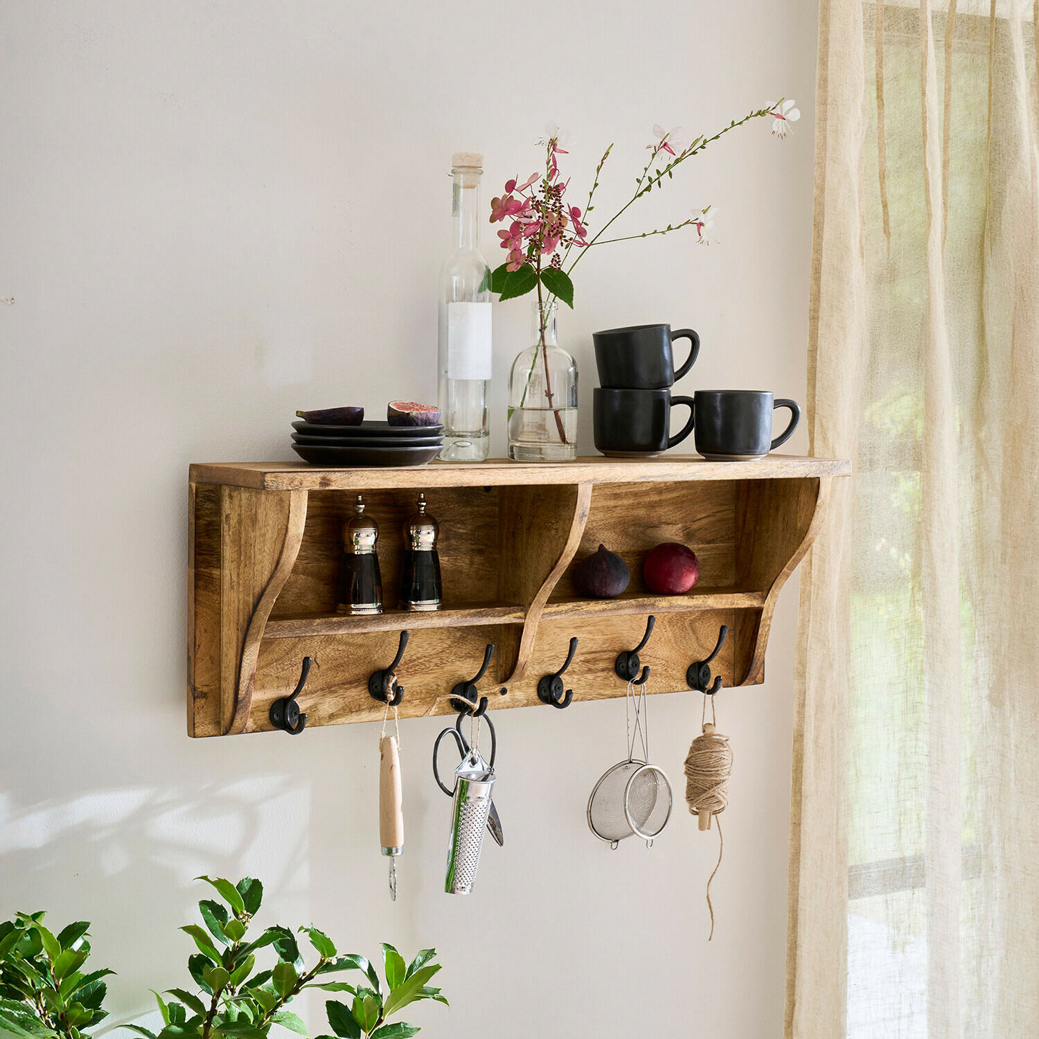 Wandregal Farrowby Wandregal aus Holz mit Haken, schwarzen Tassen, Tellern und Blumenarrangement in hellem Raum
