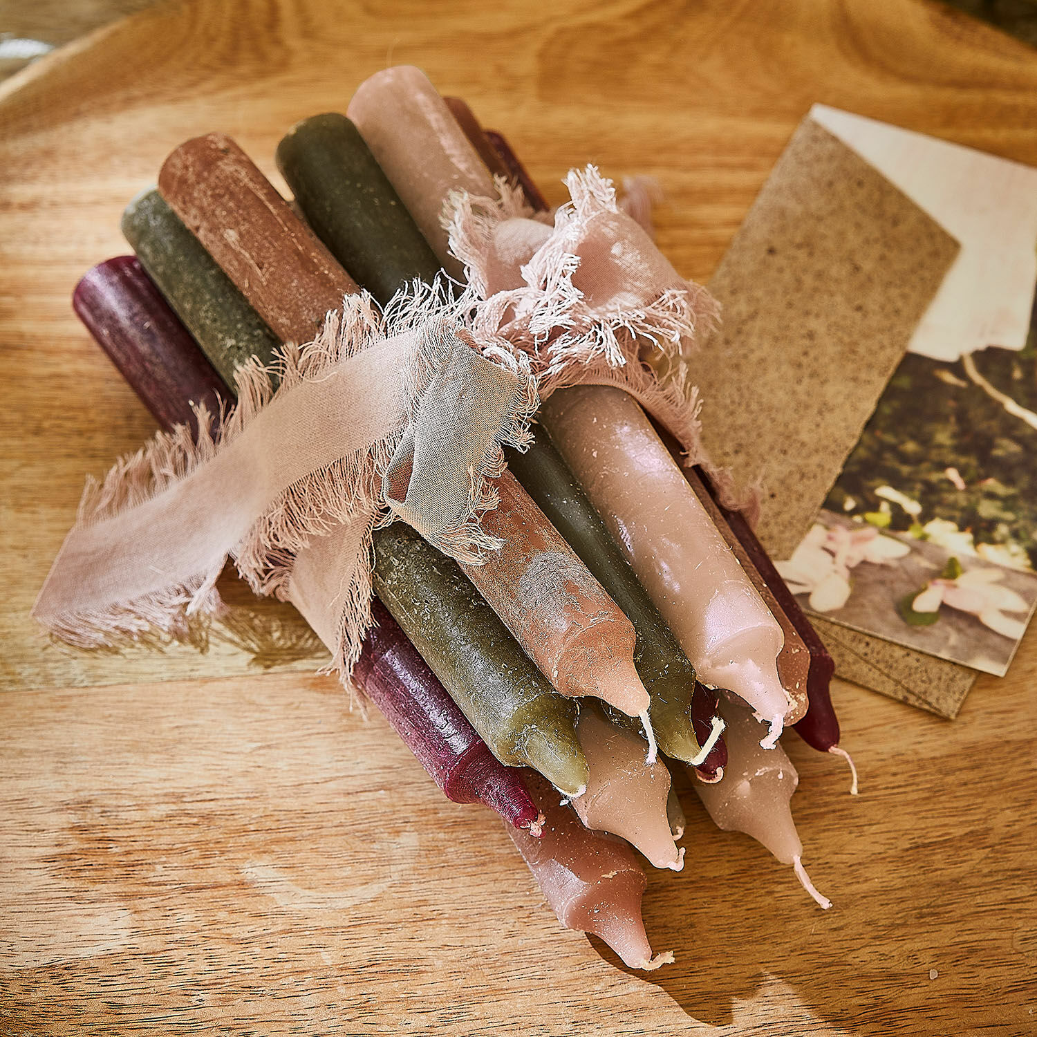 Bündel bunter Stabkerzen aus Naturwachs mit rosa Band auf Holztisch gebunden