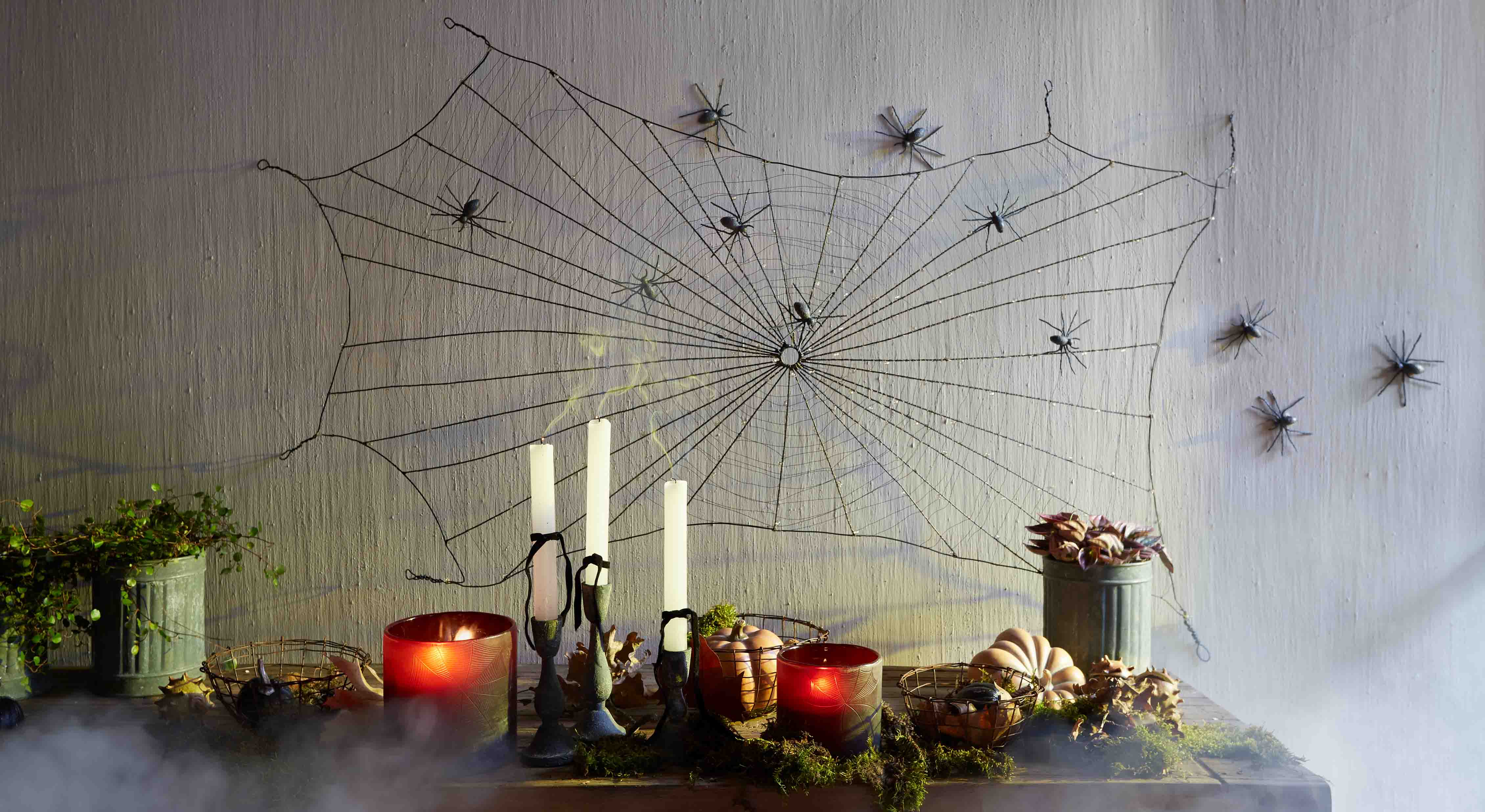 Halloween-Dekoration mit schwarzem Spinnennetz und Plastikspinnen an der Wand, Kerzen und Kürbisse auf dem Tisch