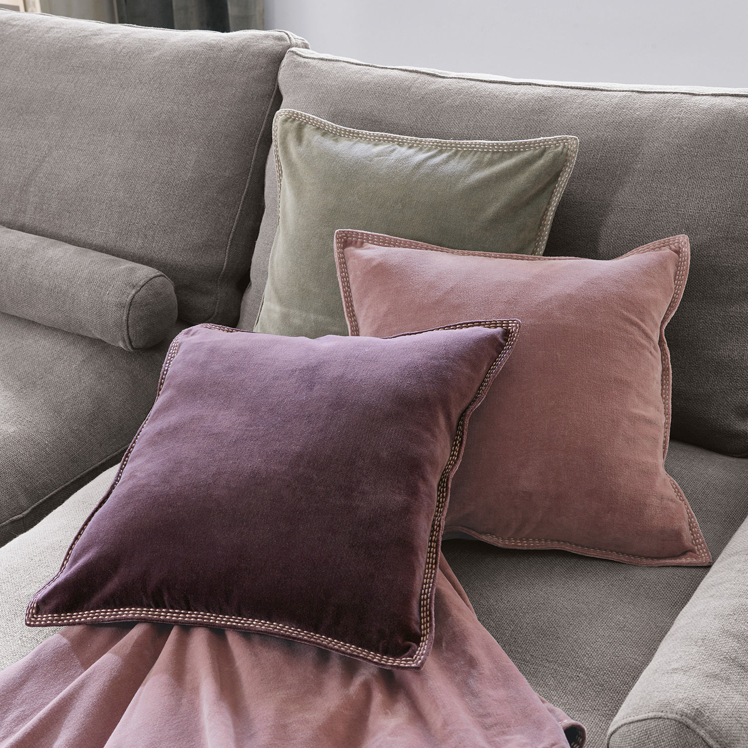 Kissen 3er Set Allonnes Drei samtige Kissen in Violett, Rosa und Grün auf grauem Sofa arrangiert