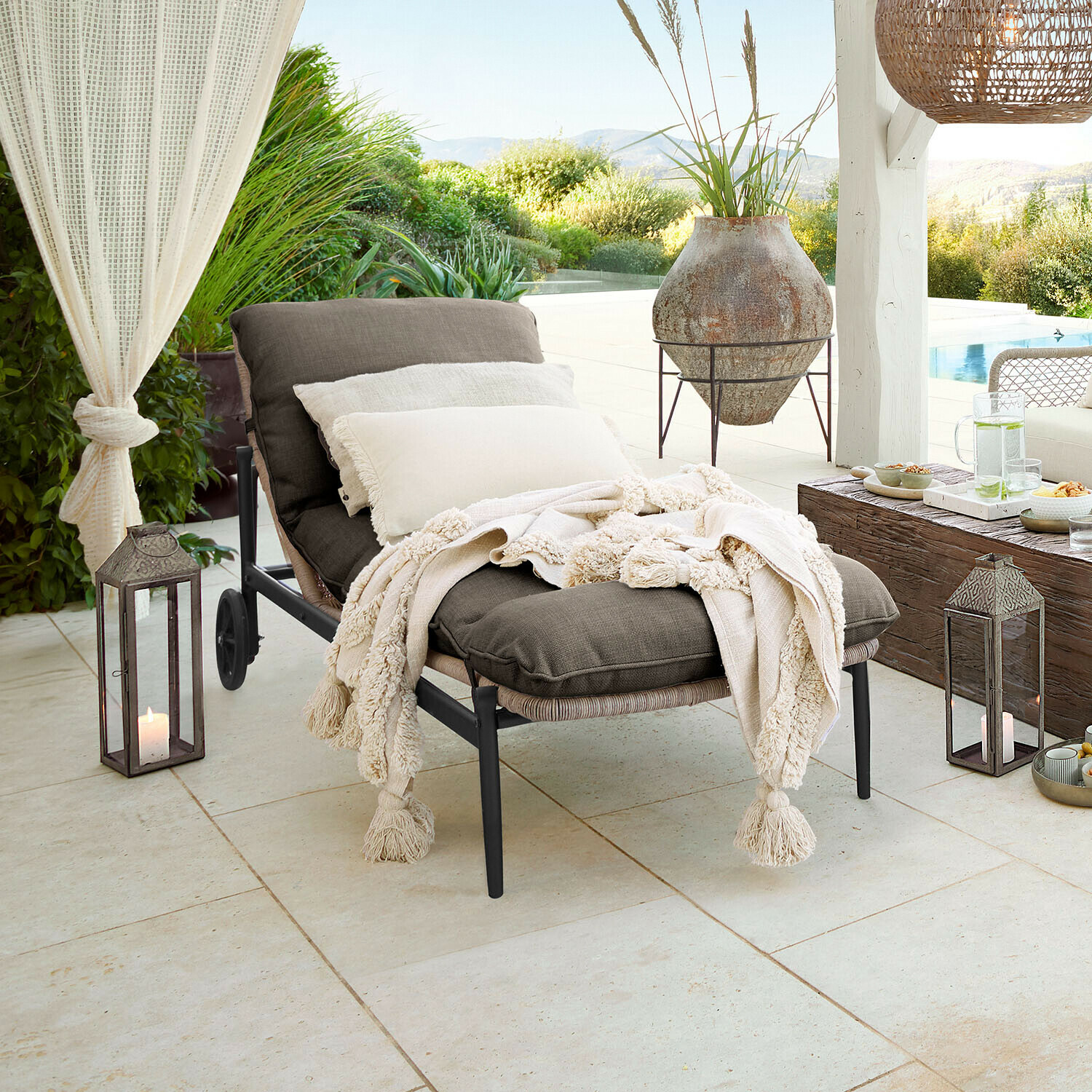 Lounger Langforda Gartenliege mit dunkelgrauem Stoff und cremefarbenem Fransenplaid auf Terrasse mit Gartenblick