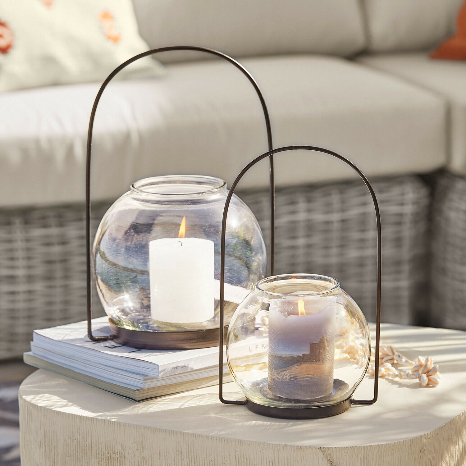 Zwei Glaslaternen mit Metallgriffen und brennenden Kerzen auf hellem Dekotisch