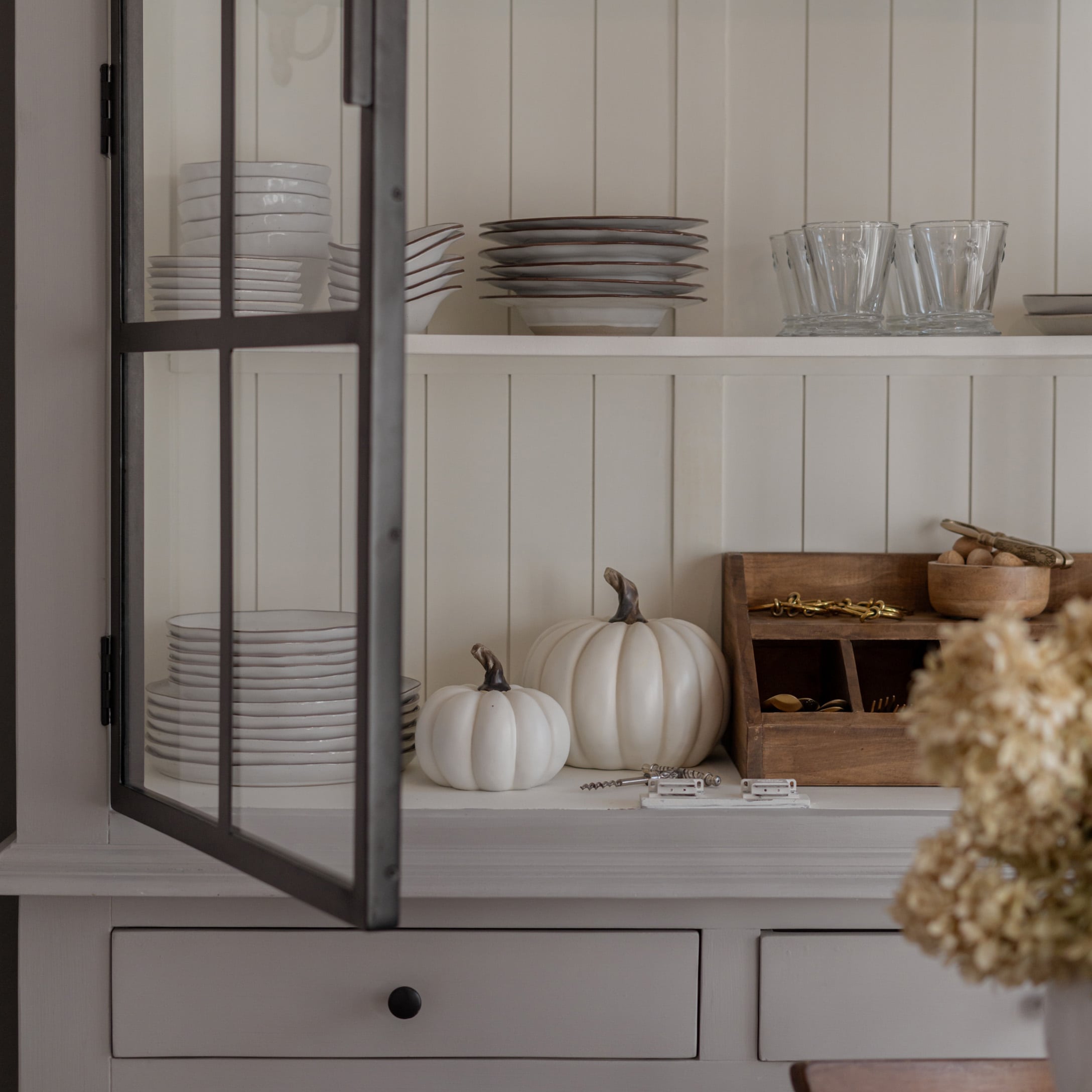 Weiße Keramikteller und Gläser auf Regal mit dekorativen weißen Kürbissen und Holz-Organizer