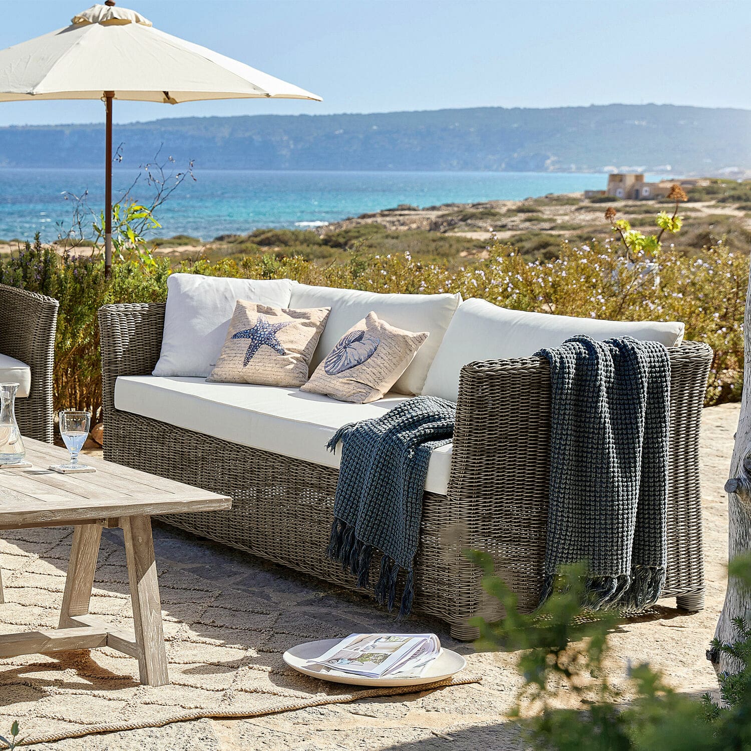 Sofa Graves Gartensofa aus grauem Rattan mit weißen Kissen und maritimen Dekokissen für Terrasse am Meer