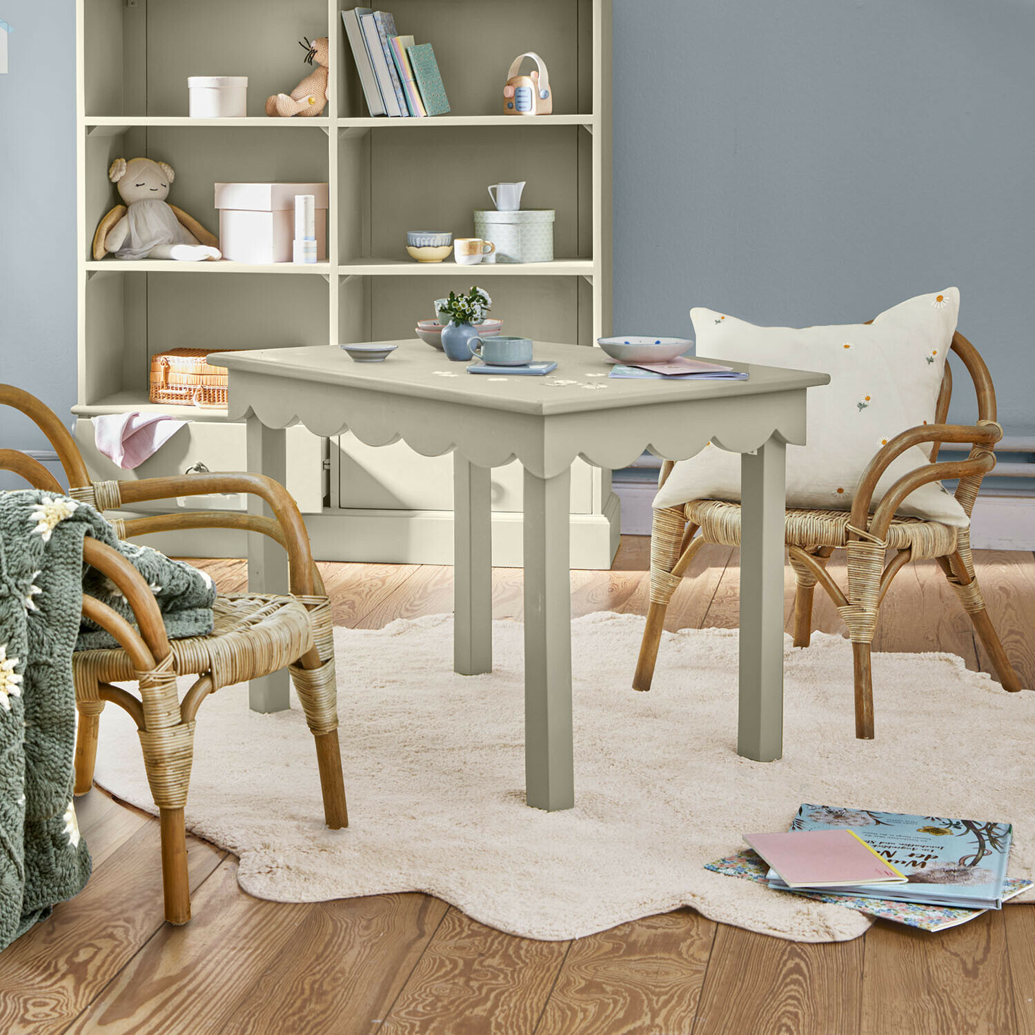 Grauer Kindertisch aus Holz mit wellenförmiger Kante auf hellem Teppich in Raum mit Rattanstühlen